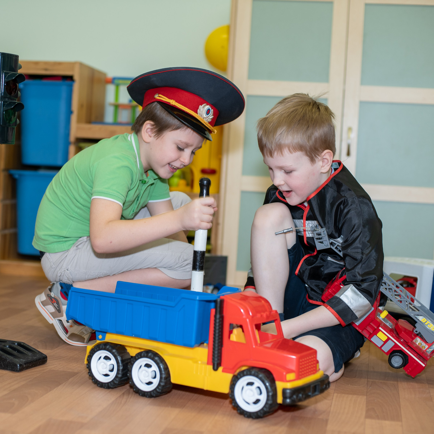 Игры в детском саду. Мальчики играют с большой машиной. Мальчик в фуражке полицейского.