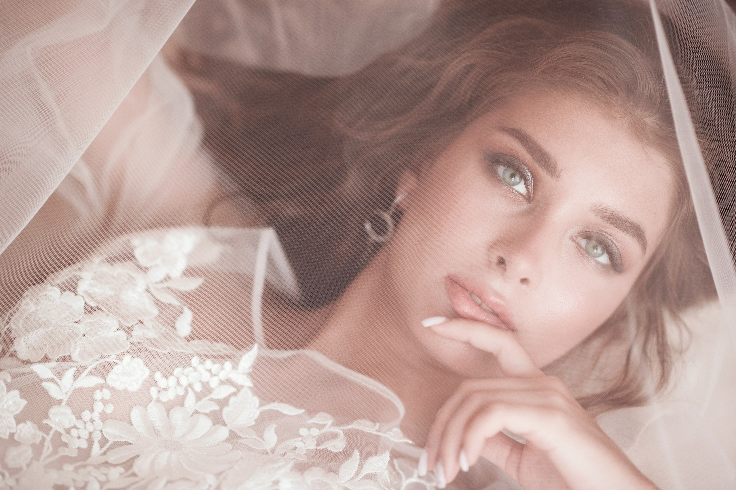 Фотография красивой невесты, которая лежит на кровати и ее лицо накрыто фатой.