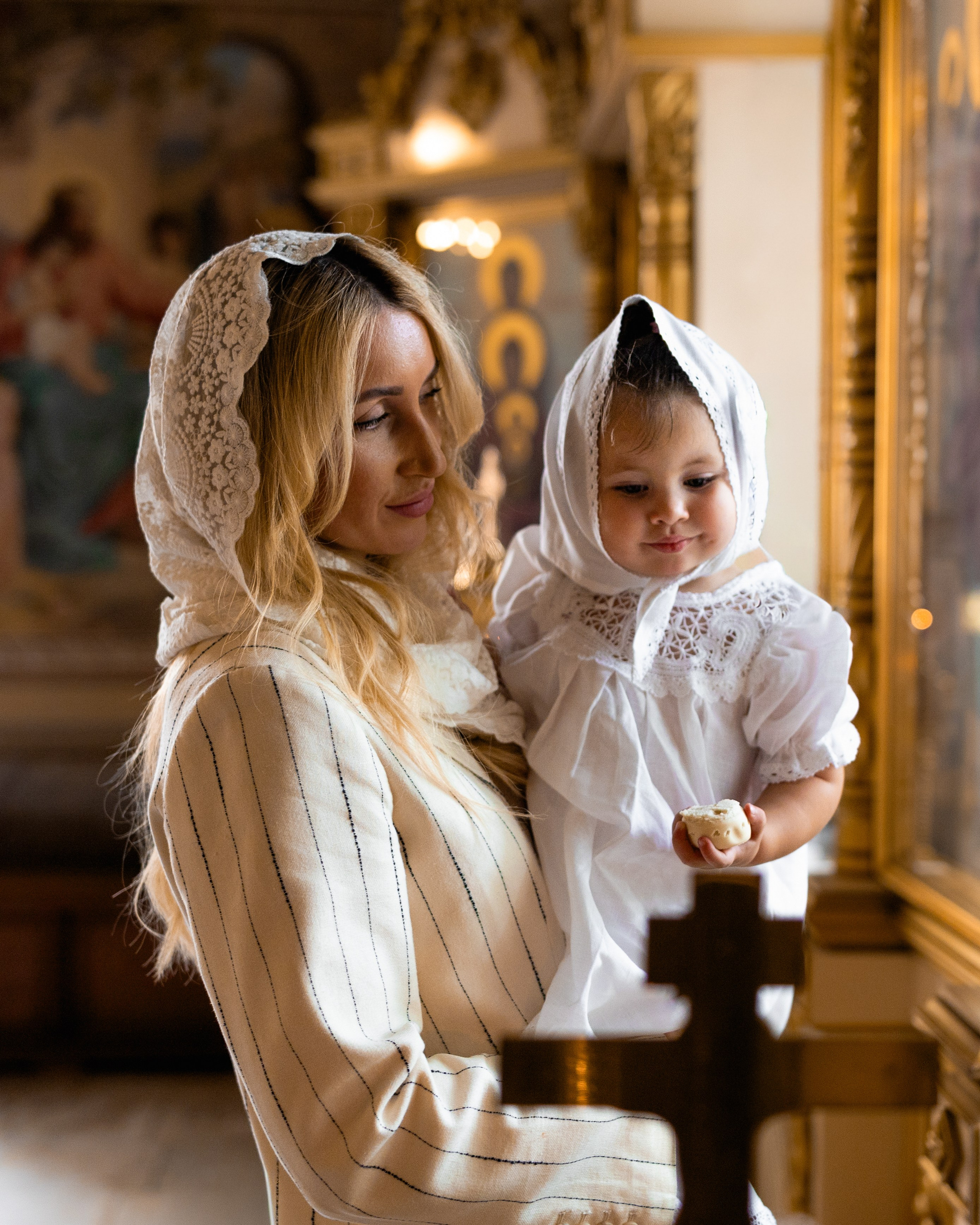 Мама держит на руках дочку в храме около окна