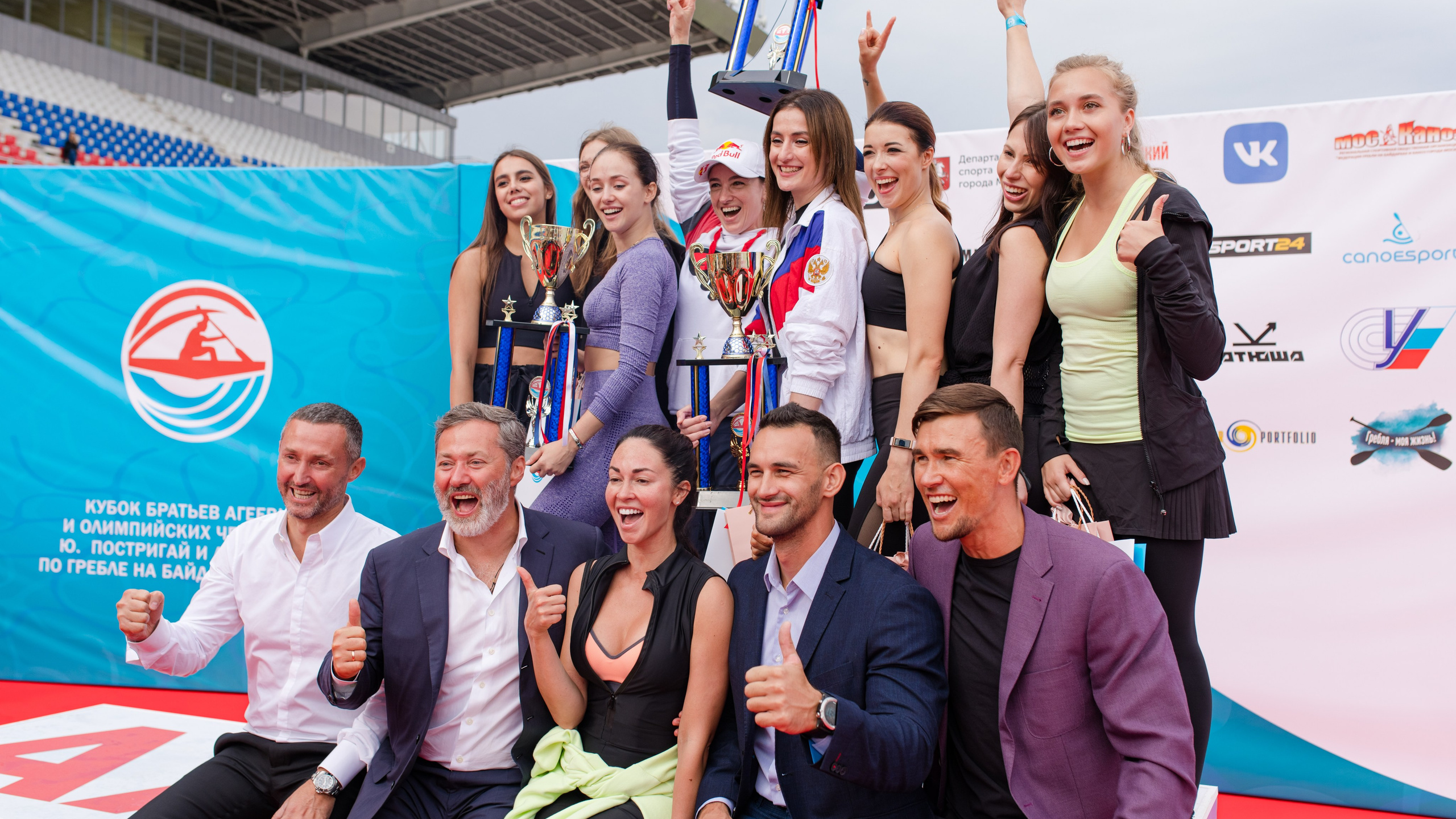 группа спортсменов на пьедестале с наградами весело улыбаются прессе