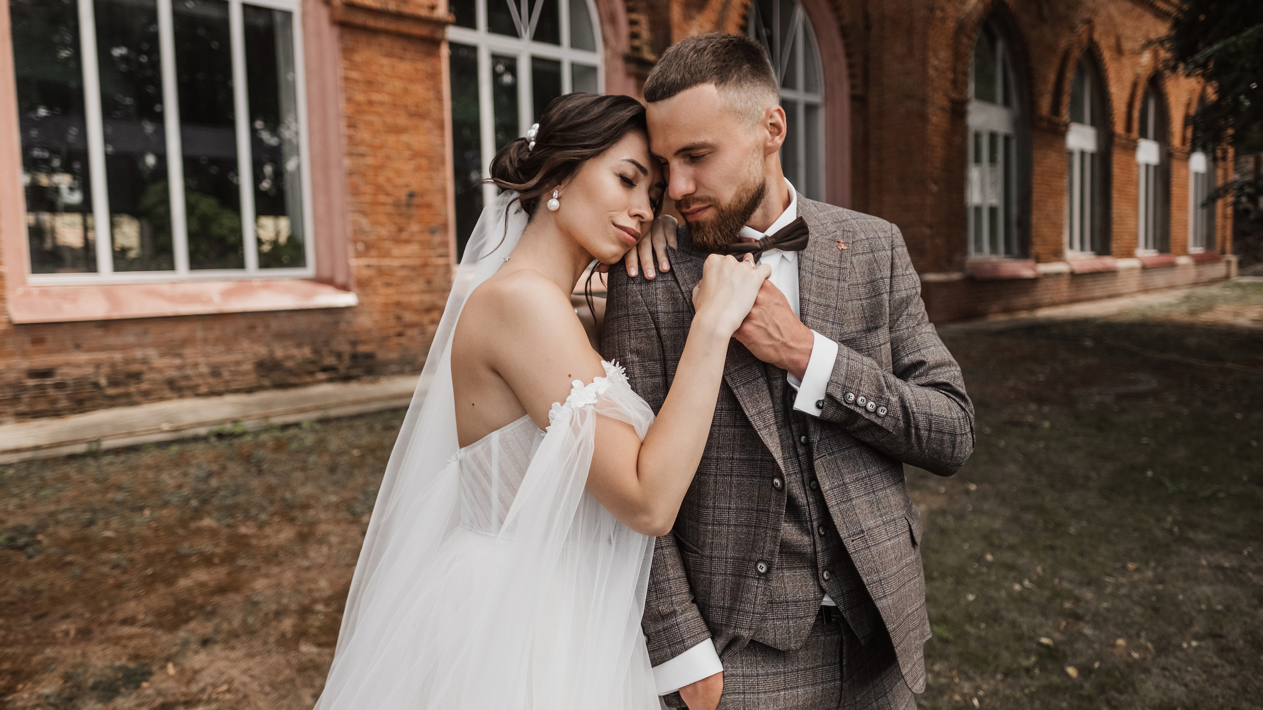 Свадебный день влюбленной пары, которые нежно склонили головы друг к другу на фоне красного кирпичного здания в Ульяновске.