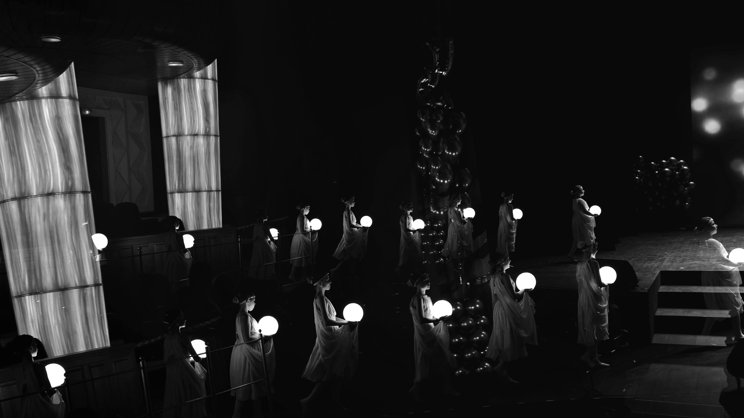 Группа танцоров в белых платьях держащих светящиеся сферы на темной сцене, многоуровневая композиция, ритуальный танец