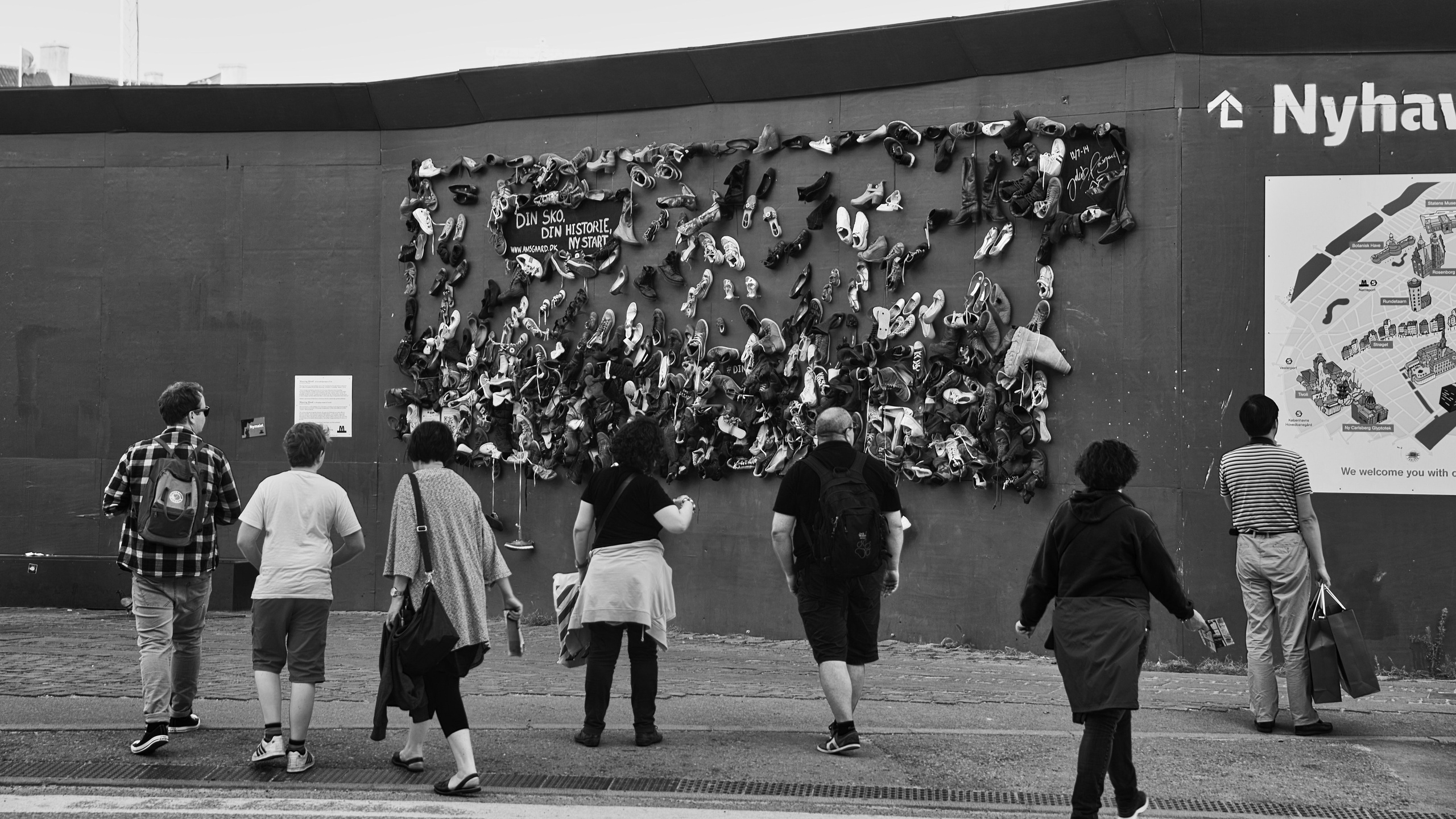 Черно-белая уличная фотография: люди смотрят на инсталляцию из обуви на стене в Нюхавне, Копенгаген, туристы, документальная съёмка, арт-объект