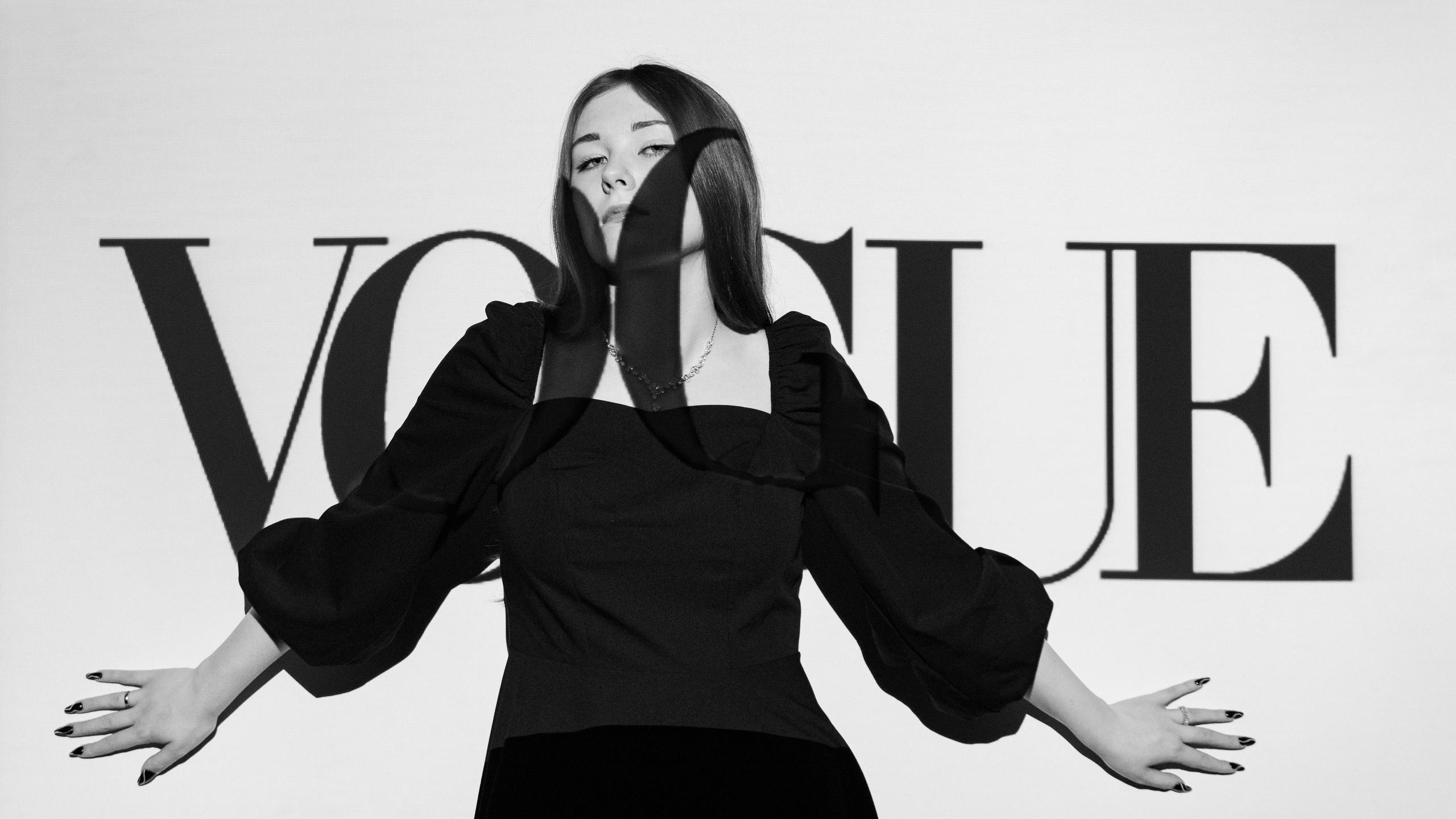Молодая девушка в черном платье позирует на фоне VOGUE