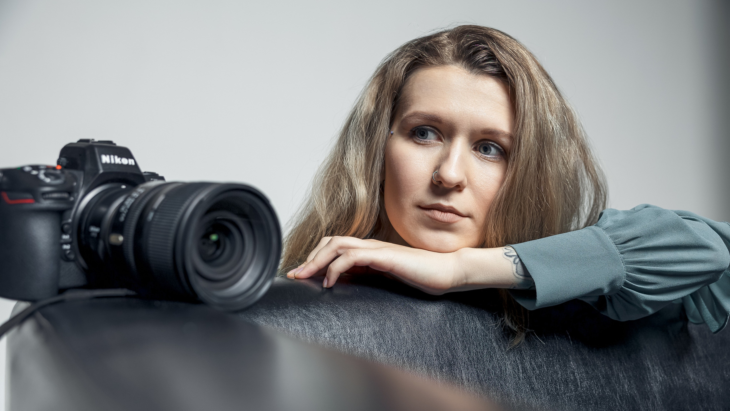 девушка с фотоаппаратом  сидит за диваном, фотоаппарат стоит на диване 