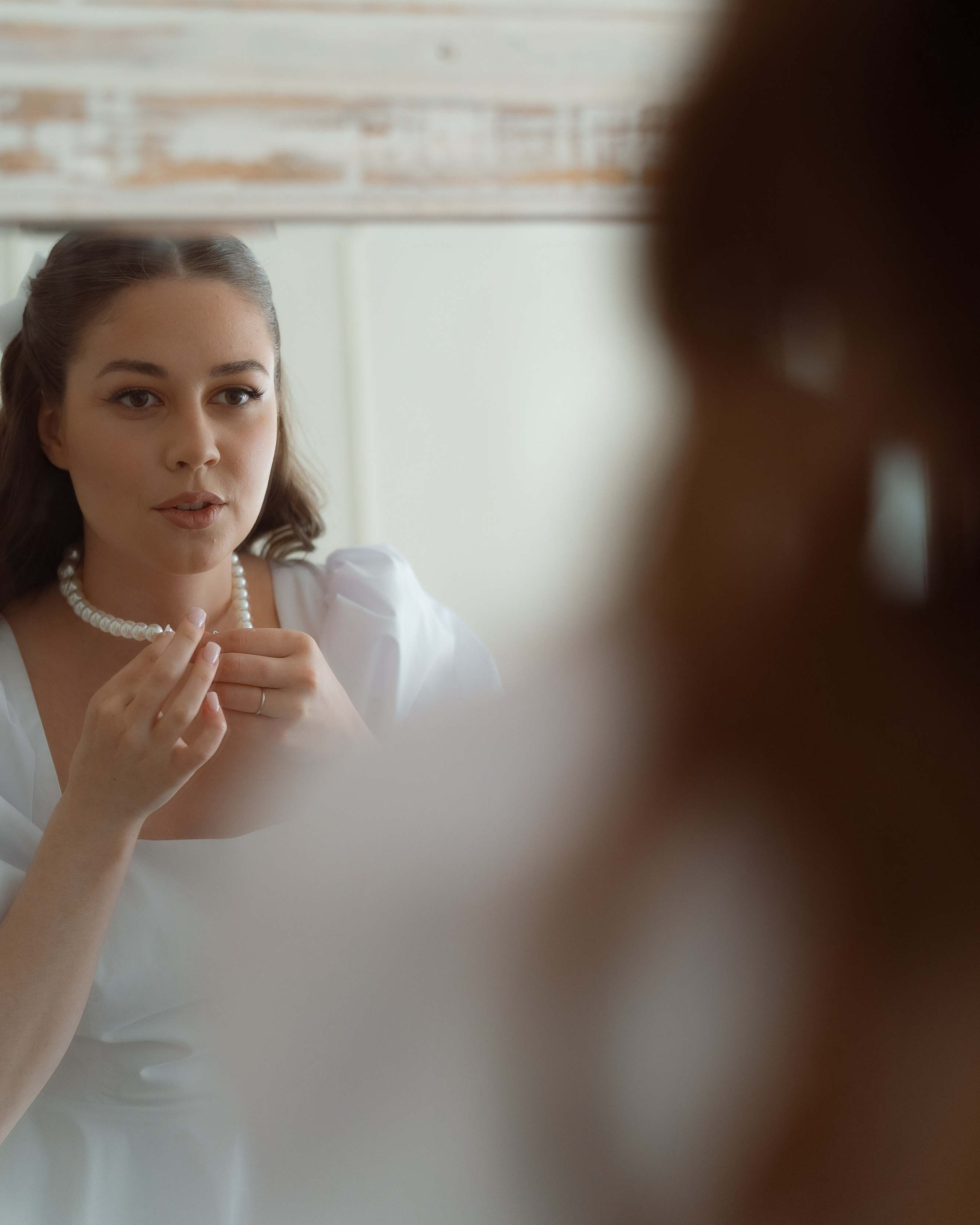 Невеста у зеркала надевает украшения утром свадьбы