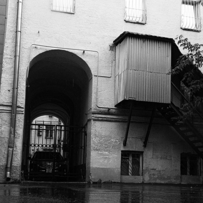 Черно-белая фотография московского двора с аркой и металлической лестницей в дождь. Городская атмосфера, трещины в стенах, отражение на мокром асфальте. Фотография-история от Вадима Топорёнка, фиксирующего моменты, когда вы можете просто быть собой