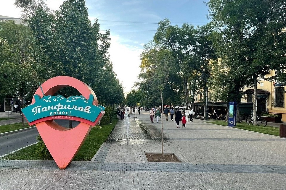 Женщина идет по тропе среди красных скал в пустынной местности. Небо пасмурное, создавая атмосферу спокойствия и уединенности. Вокруг величественные скальные образования Чарынского каньона с характерными слоями песчаника.