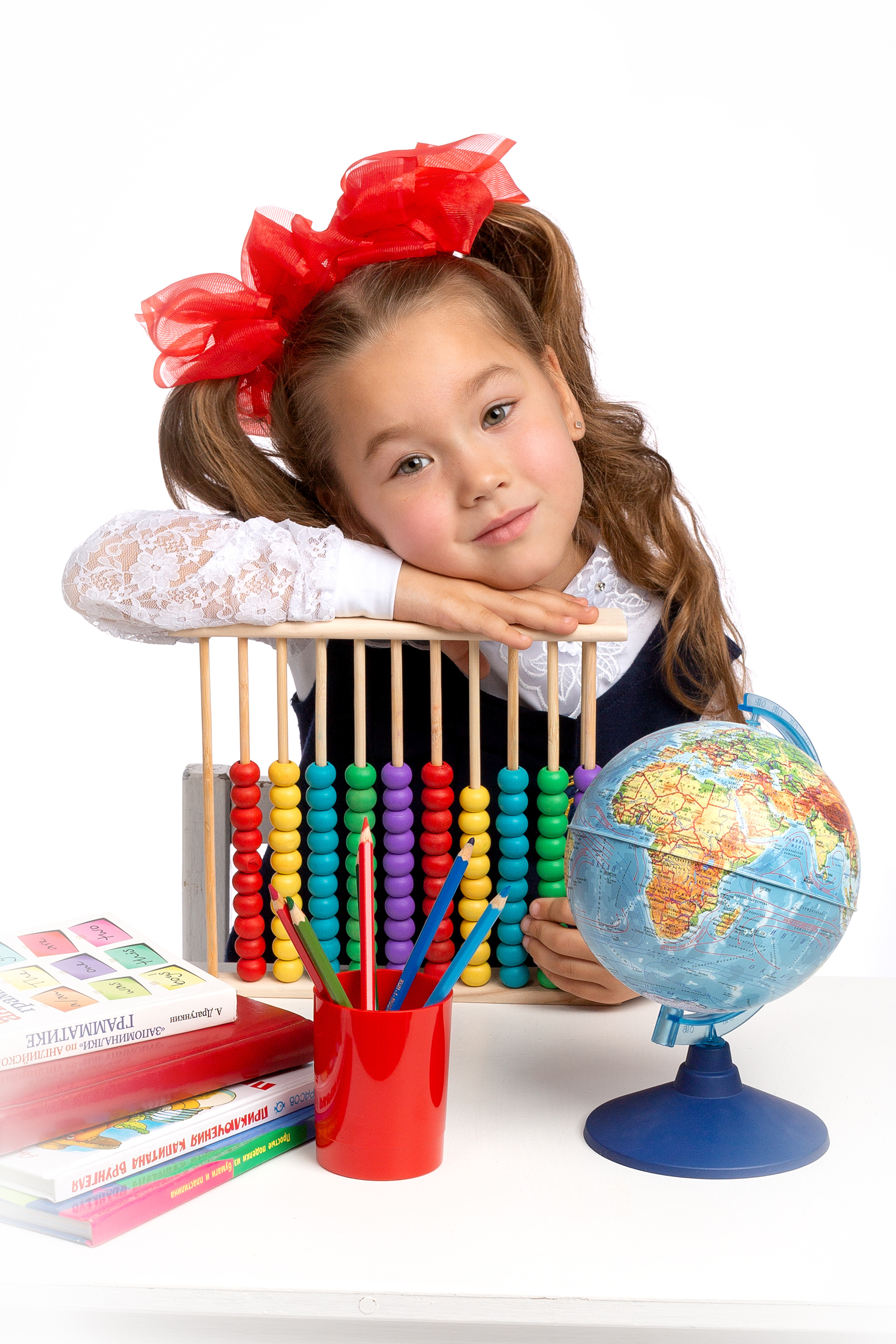 Школьные принадлежности, глобус и первоклашка составляют красивую композицию.