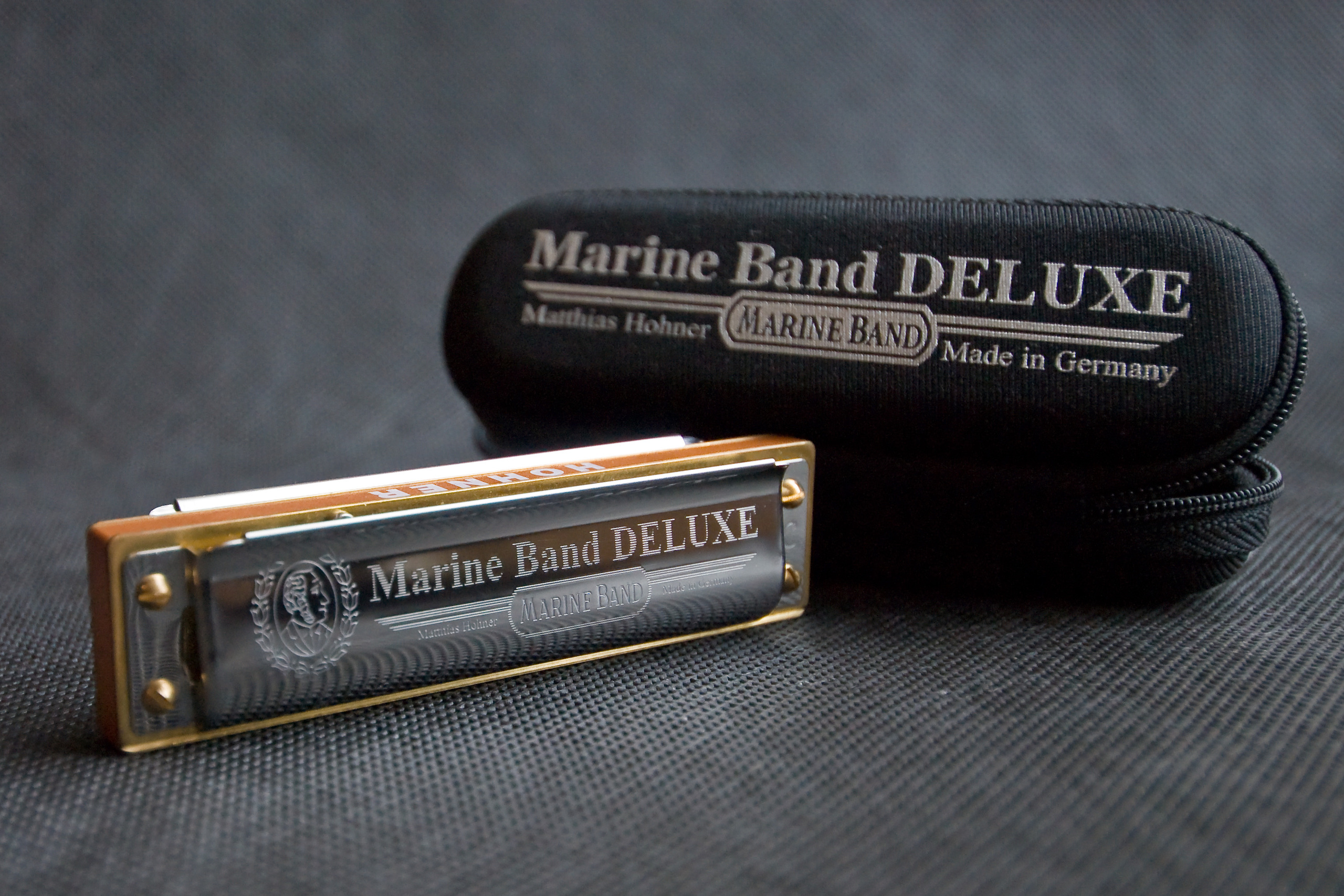 подарок для музыканта губная гармоника крупным планом с чехлом на сером фоне