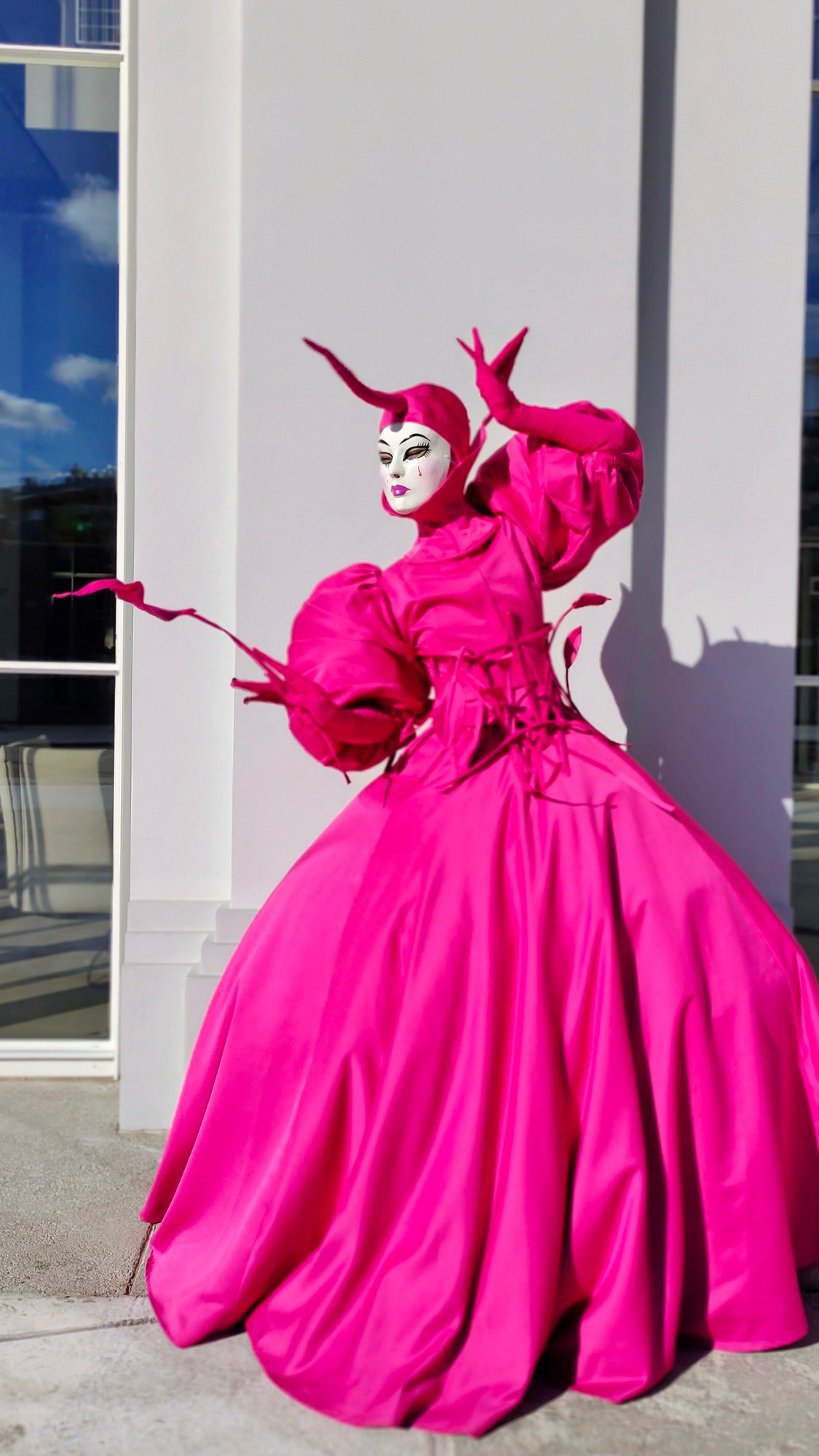 Артист мим Фуксия стоит у белой стены, держа в руках длинный цветок