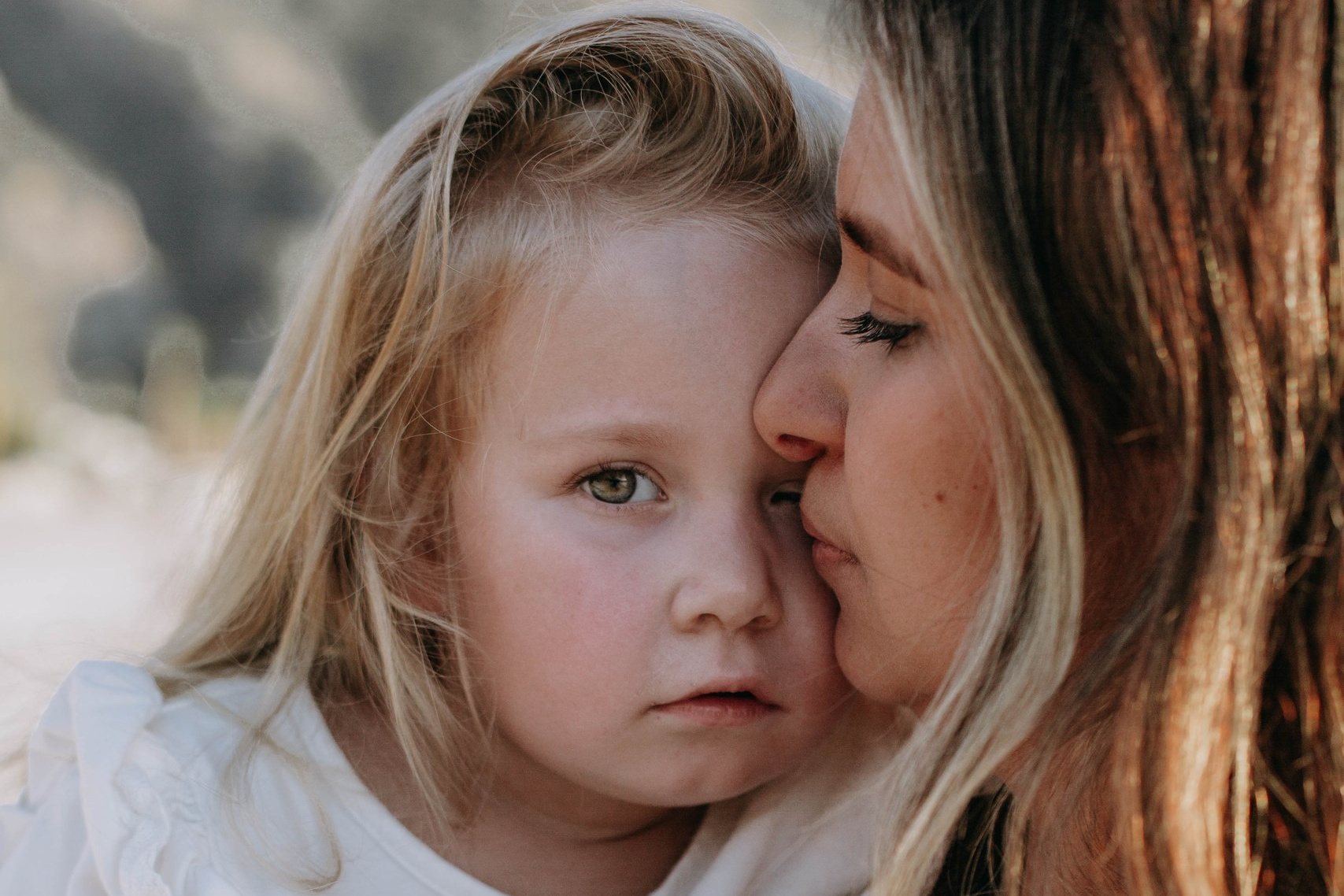 A close-up of a mother embracing her daughter, both looking calm and serene