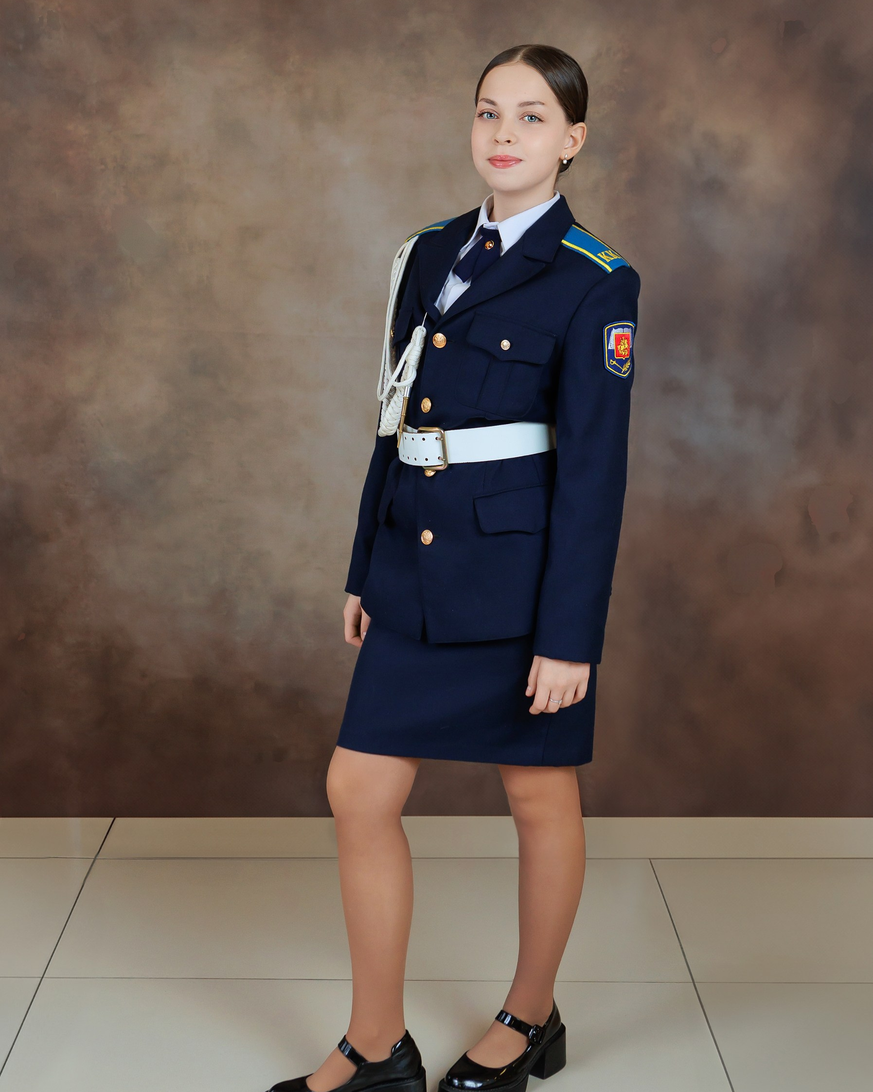Девочка в парадной синей кадетской форме на нейтральном студийном фоне.