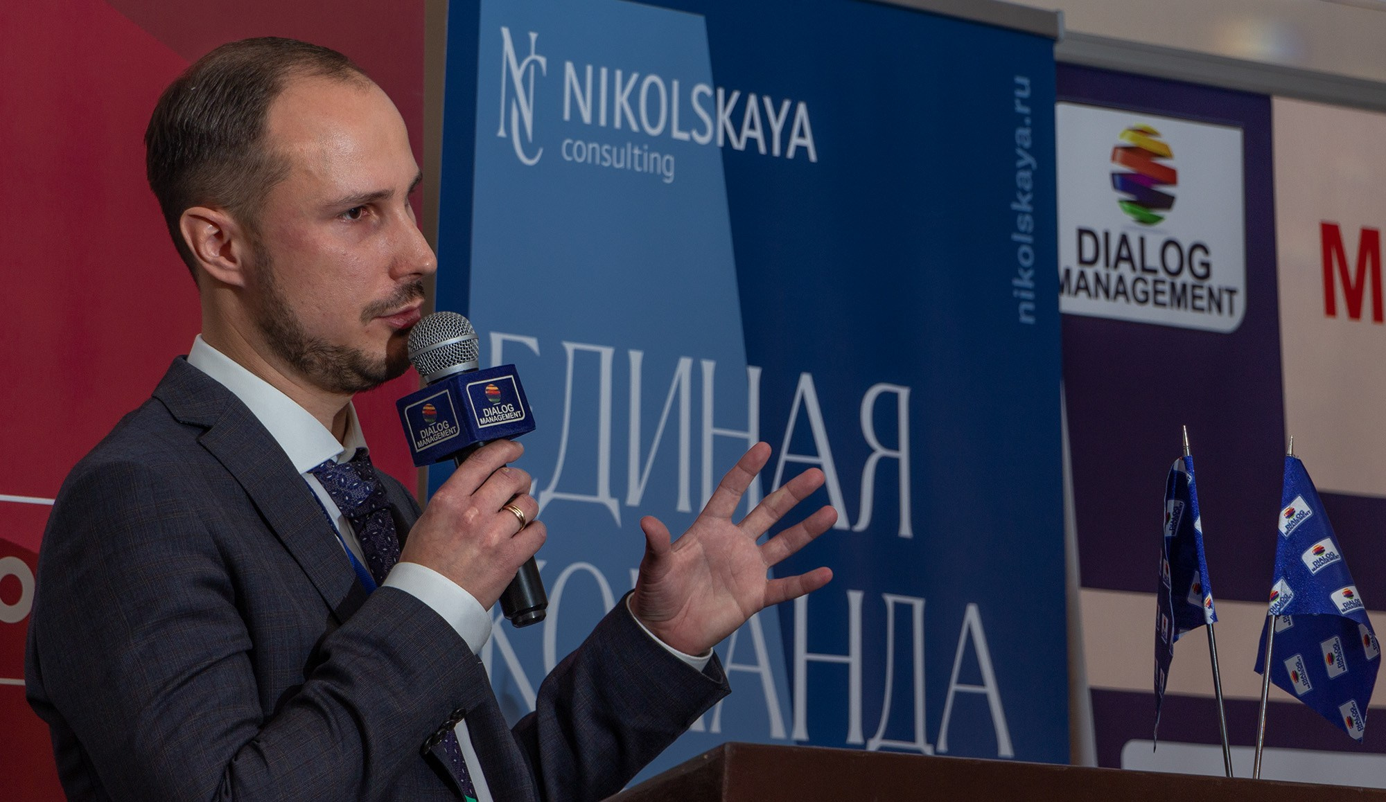 Выступление спикера у микрофона на фоне официального баннера мероприятия
