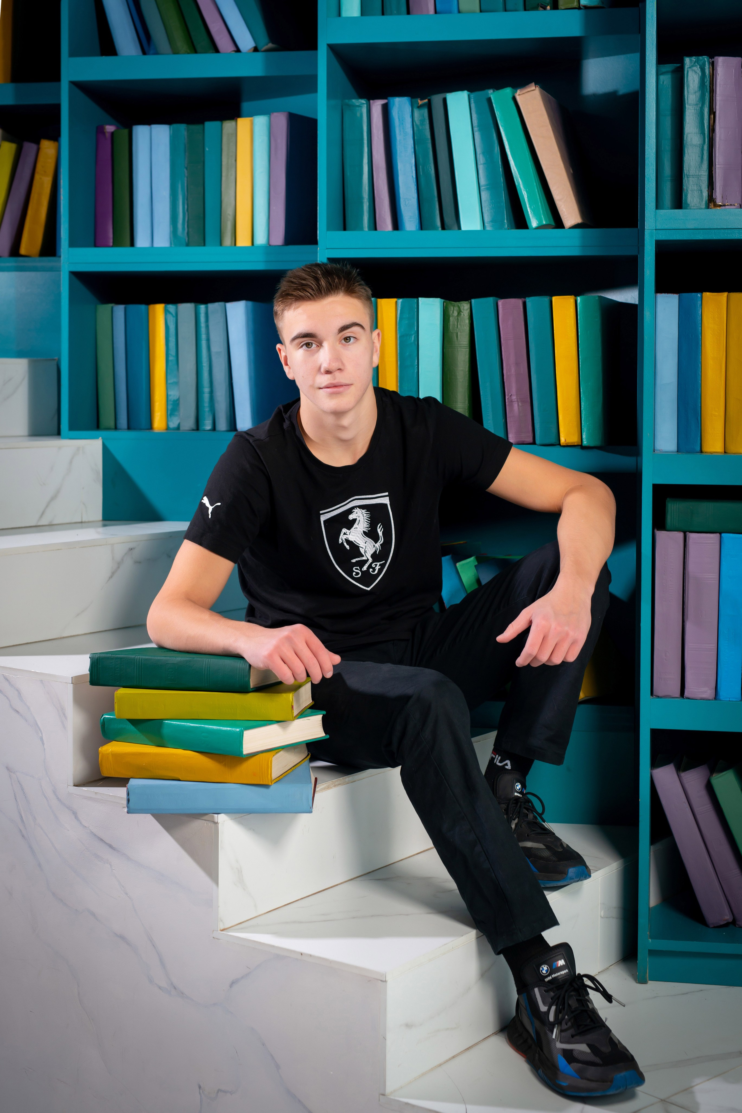 Юноша-выпускник Санкт-Петербургской гимназии позирует сидя с книгами на фотосессии для стильного выпускного фотоальбома.