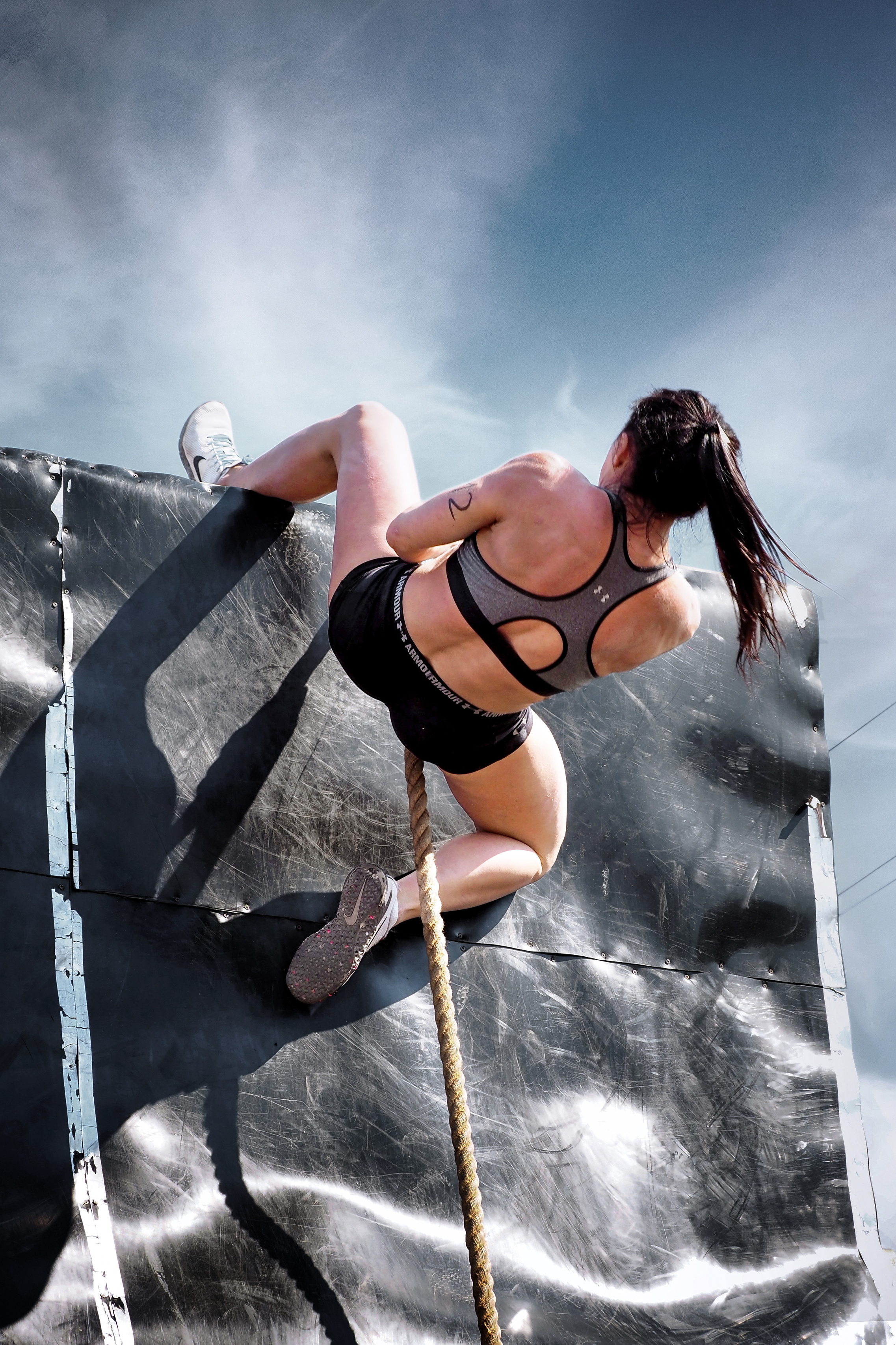 девушка-спортсменка перелезает через высокое препятствие на соревнованиях по ocr