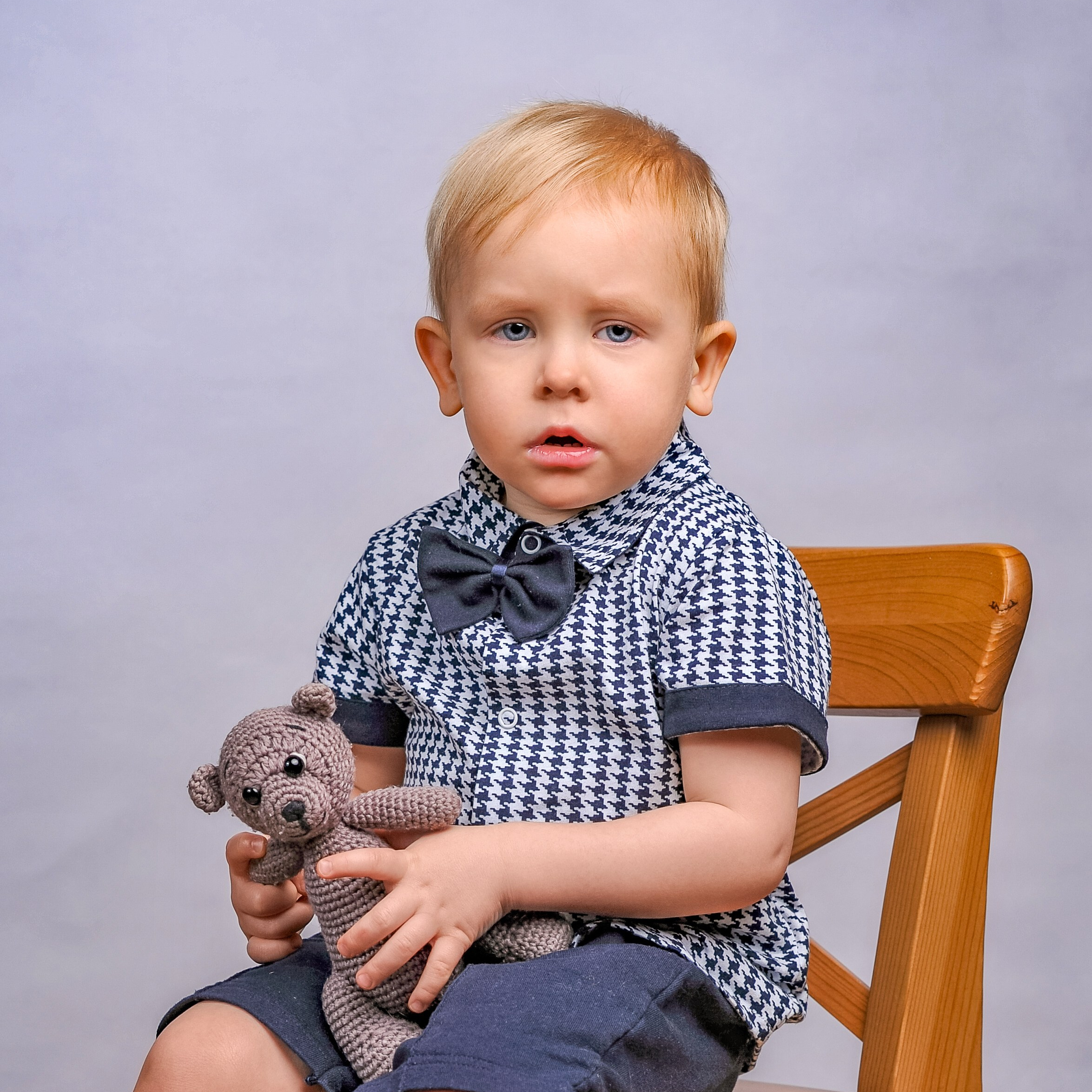 Фотосессия ясельная группа в детском саду на однотонном фоне. Мальчик на стульчике с игрушкой.