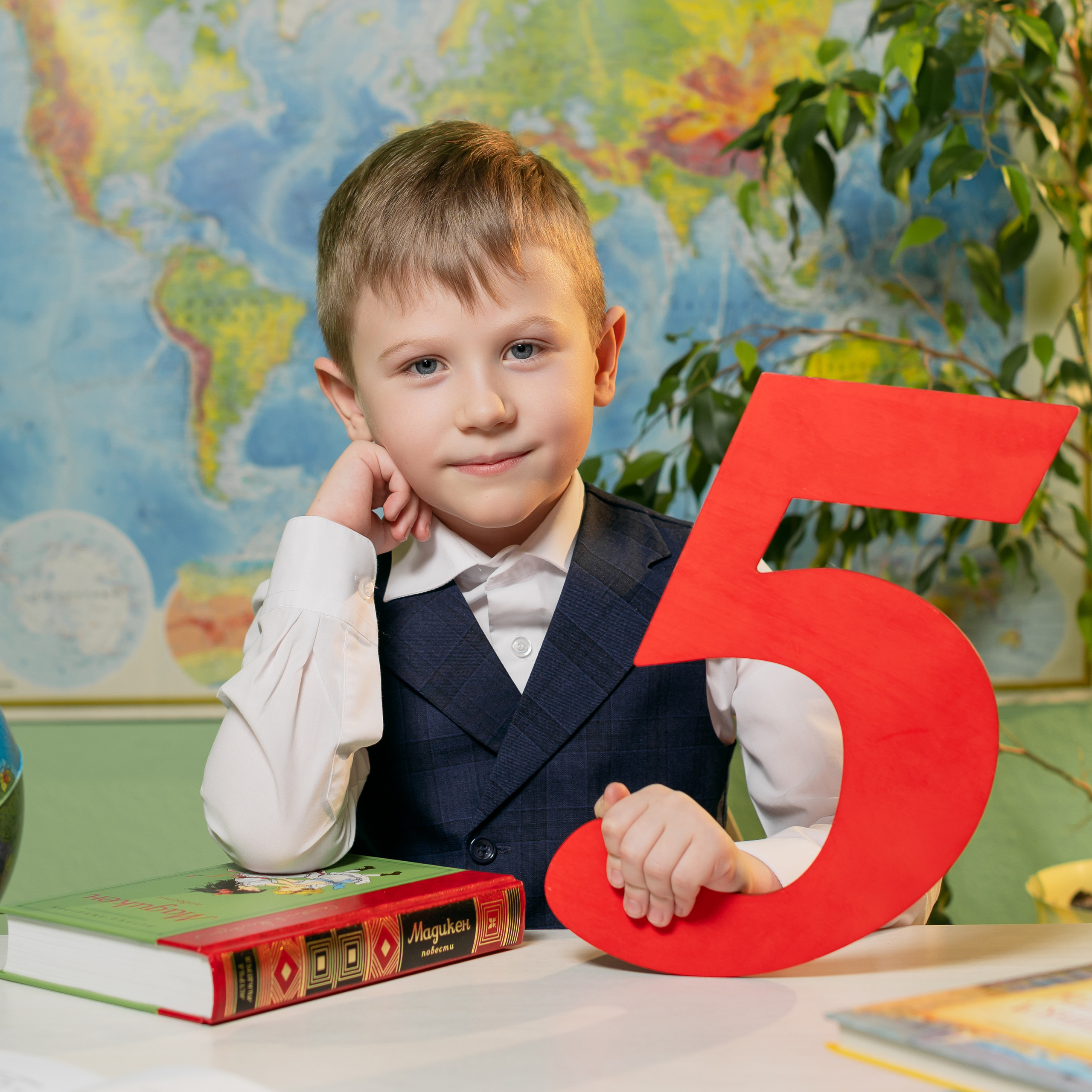 Первоклассник с пятеркой на фоне карты мира. Работа школьного фотографа студии Вышка в Москве.