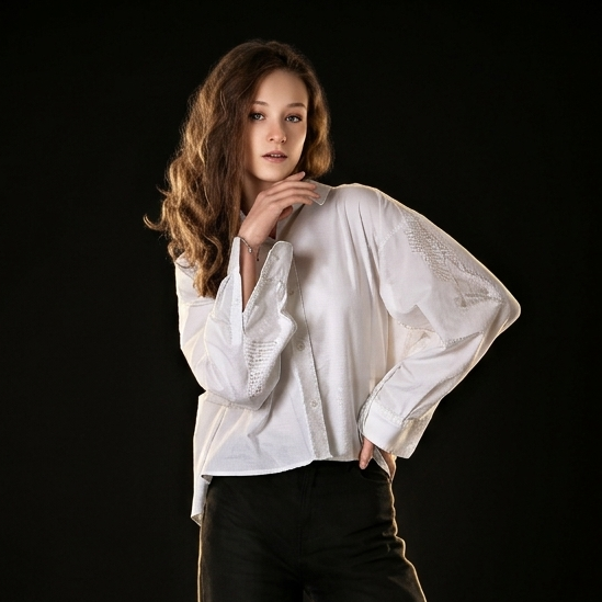 Девочка с очень длинными волнистыми светлыми волосами сидит на стуле на сером фоне.