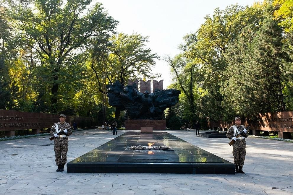 Женщина идет по тропе среди красных скал в пустынной местности. Небо пасмурное, создавая атмосферу спокойствия и уединенности. Вокруг величественные скальные образования Чарынского каньона с характерными слоями песчаника.