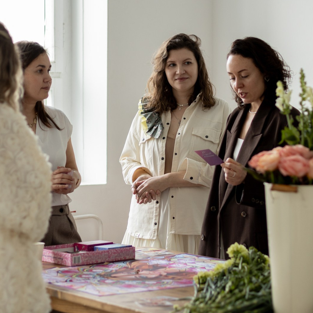 Женщина в уютной одежде держит в руках карты трансформационной игры Женское счастье, на столе горят свечи, тёплое освещение, кадр передаёт атмосферу доверия и глубины