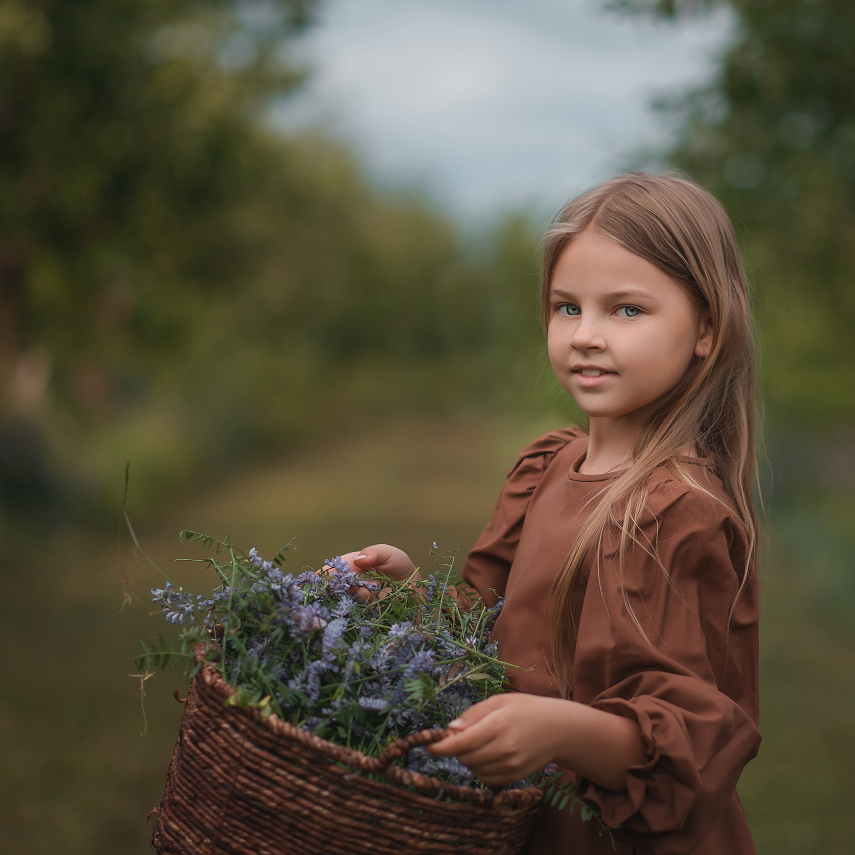 Девочка с корзинкой, наполненной цветами, в саду.
