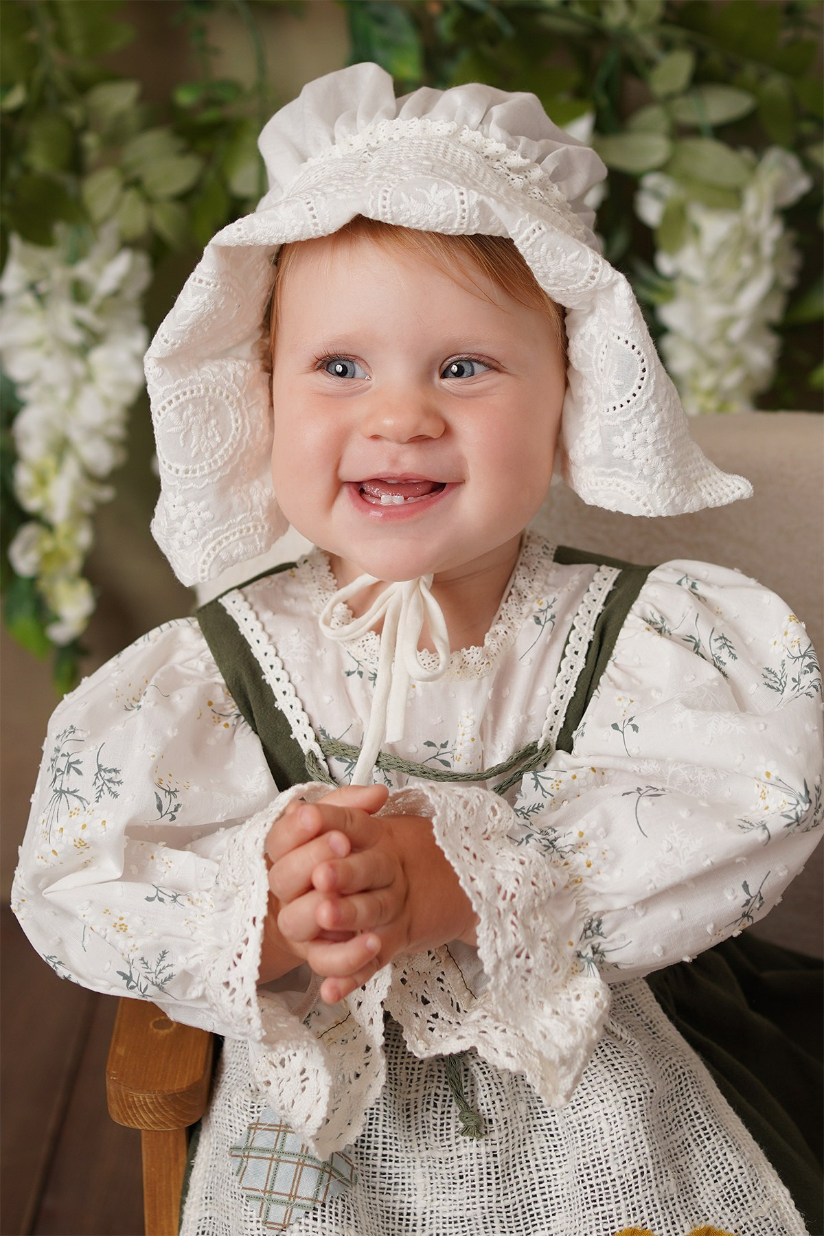 На фото портрет улыбающейся малышки в красивом зеленом платье и милом чепчике.