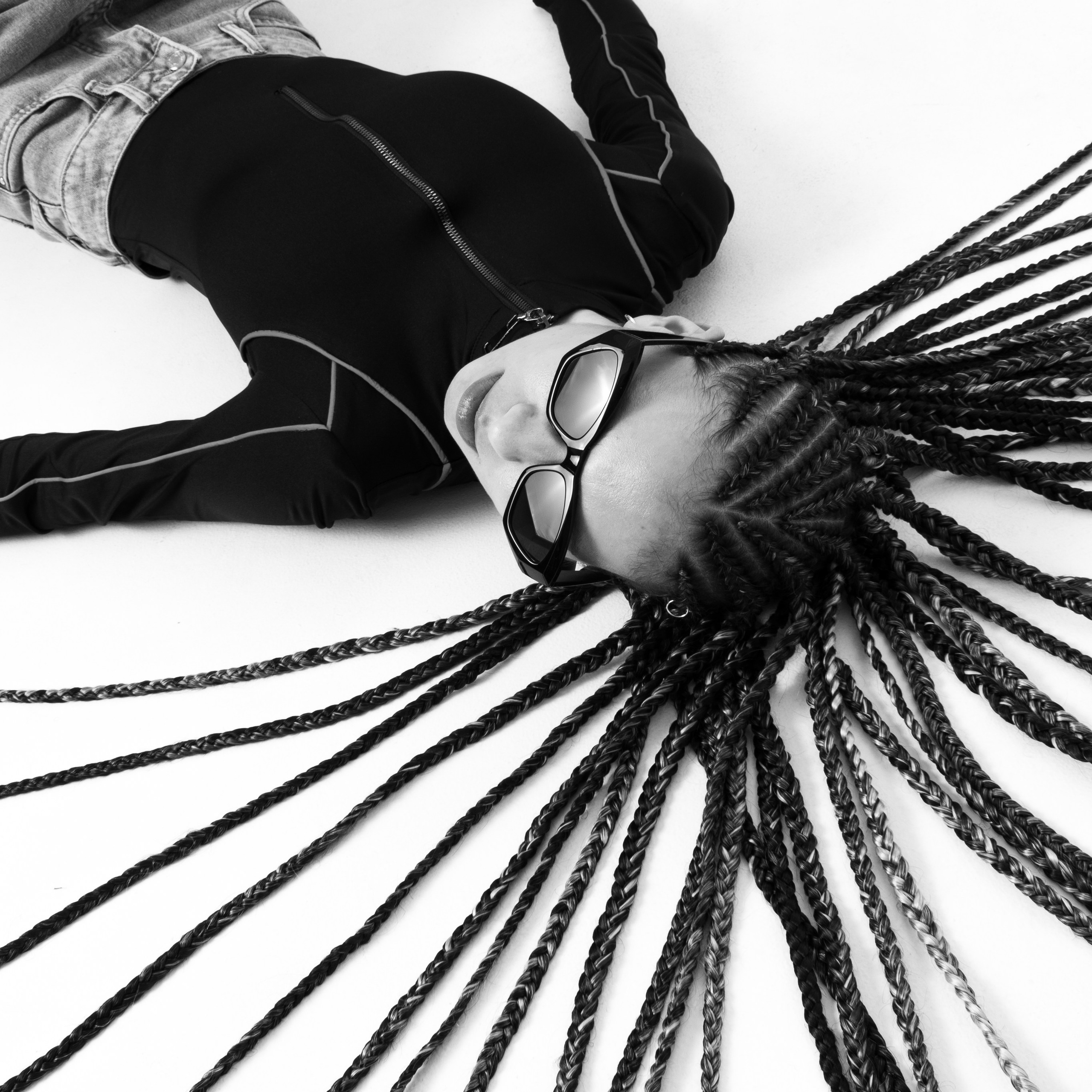 Девушка в очках с длинными косичками позирует на циклораме