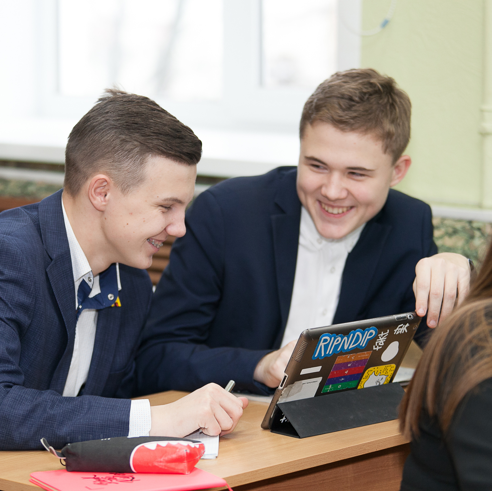 два ученика за партой с планшетом в синих костюмах улыбаются
