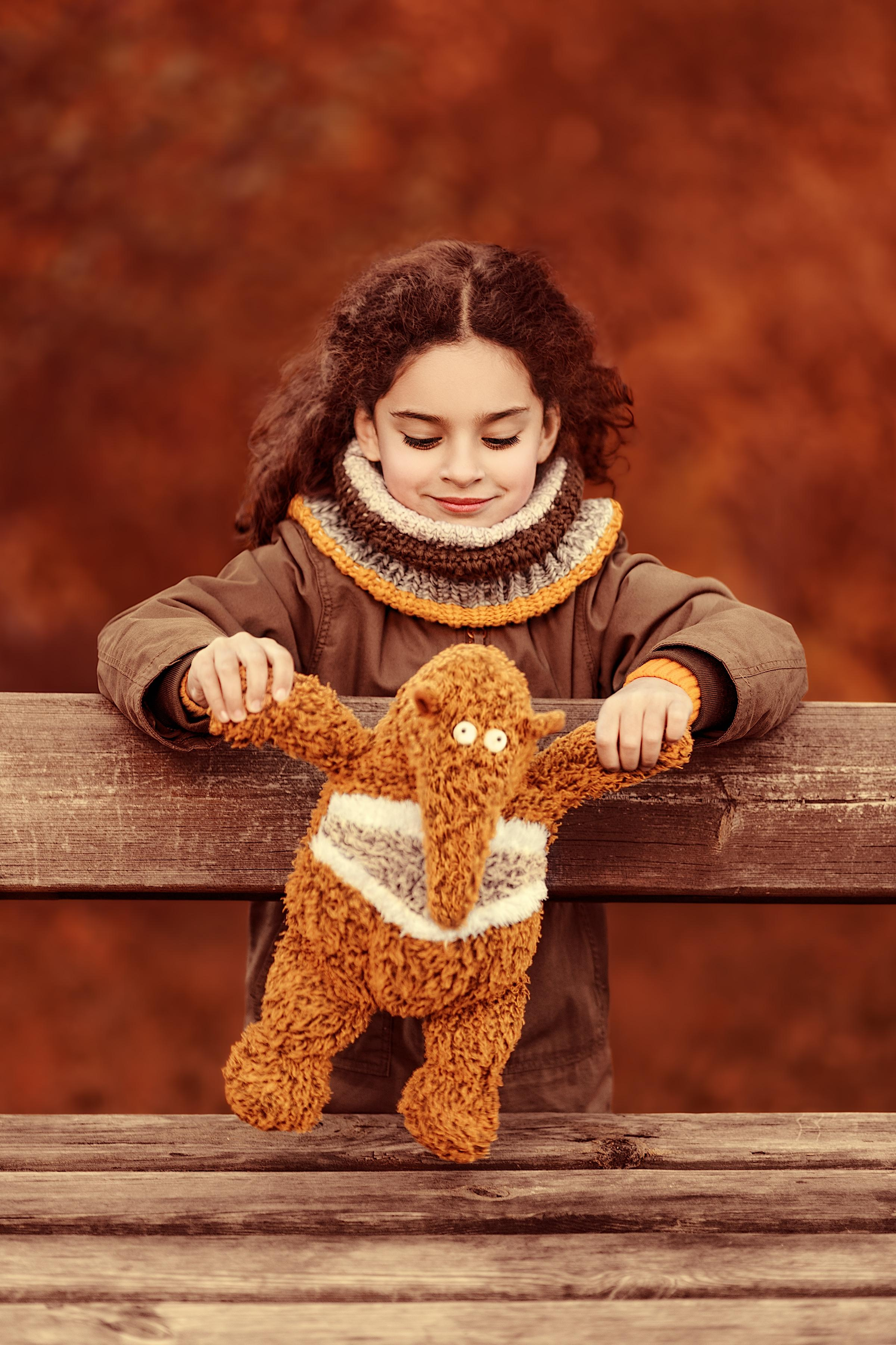 Девочка на осенней фотопрогулке играет с мягкой игрушкой Муравьедом.