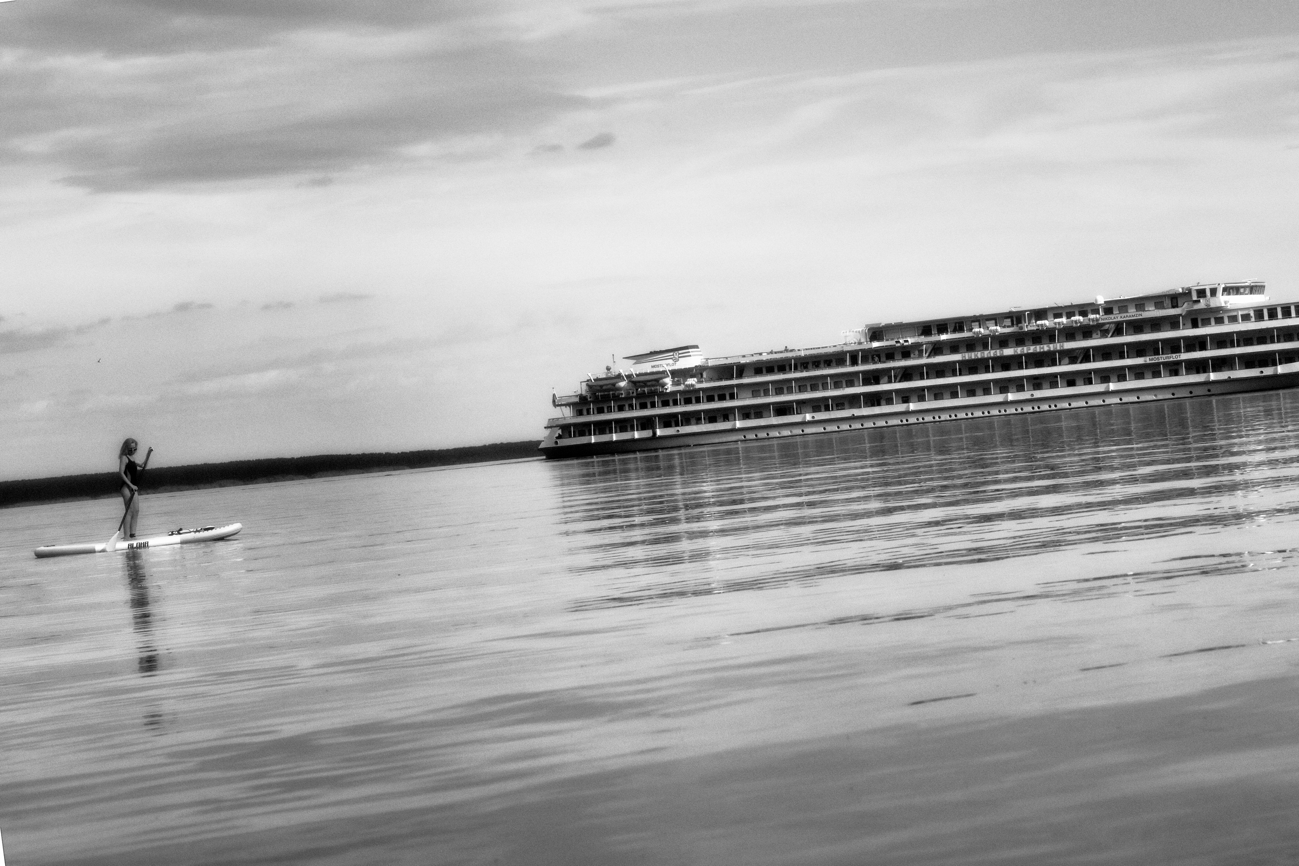 Женщина на сапе плывет рядом с огромным кораблем.