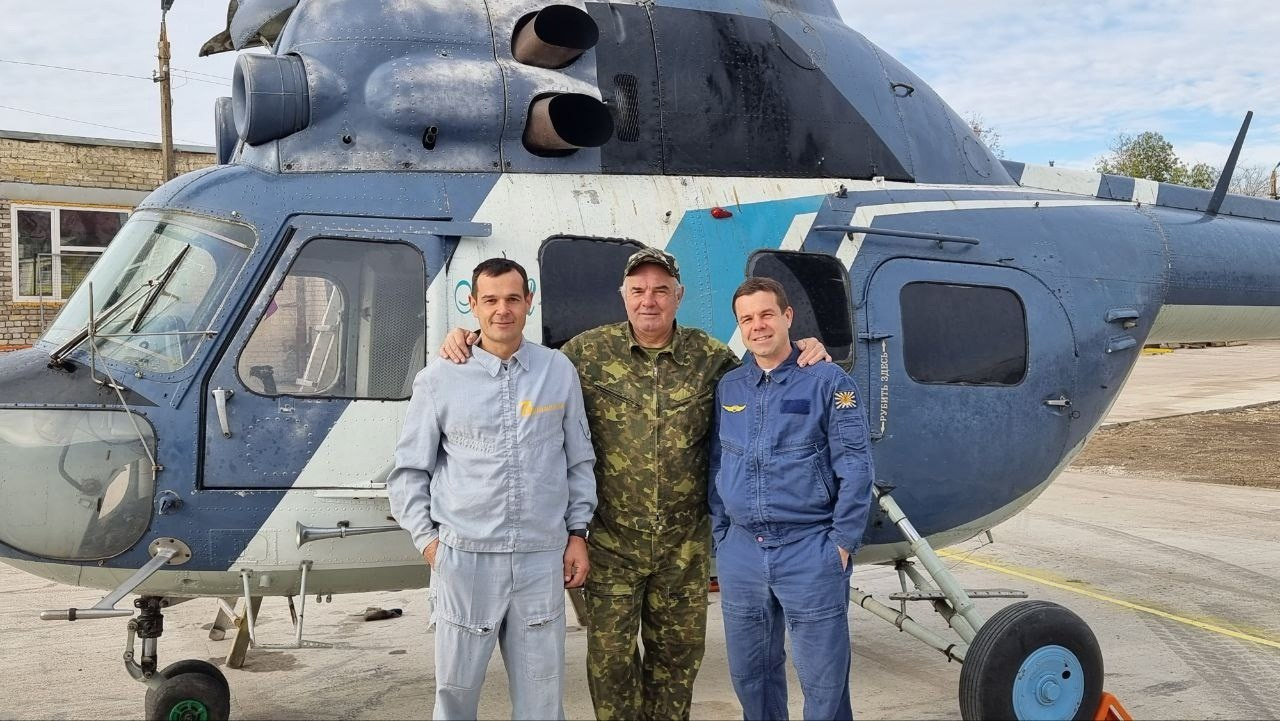 Основатели Музея вертолётов в Торжке стоят перед вертолётом Ми-2. Справа Алексей Черепнов, в центре Игорь Валентинович Черепнов, слева Александр Черепнов. Вертолёт имеет синие и белые цвета, с видимыми окнами и лопастями.