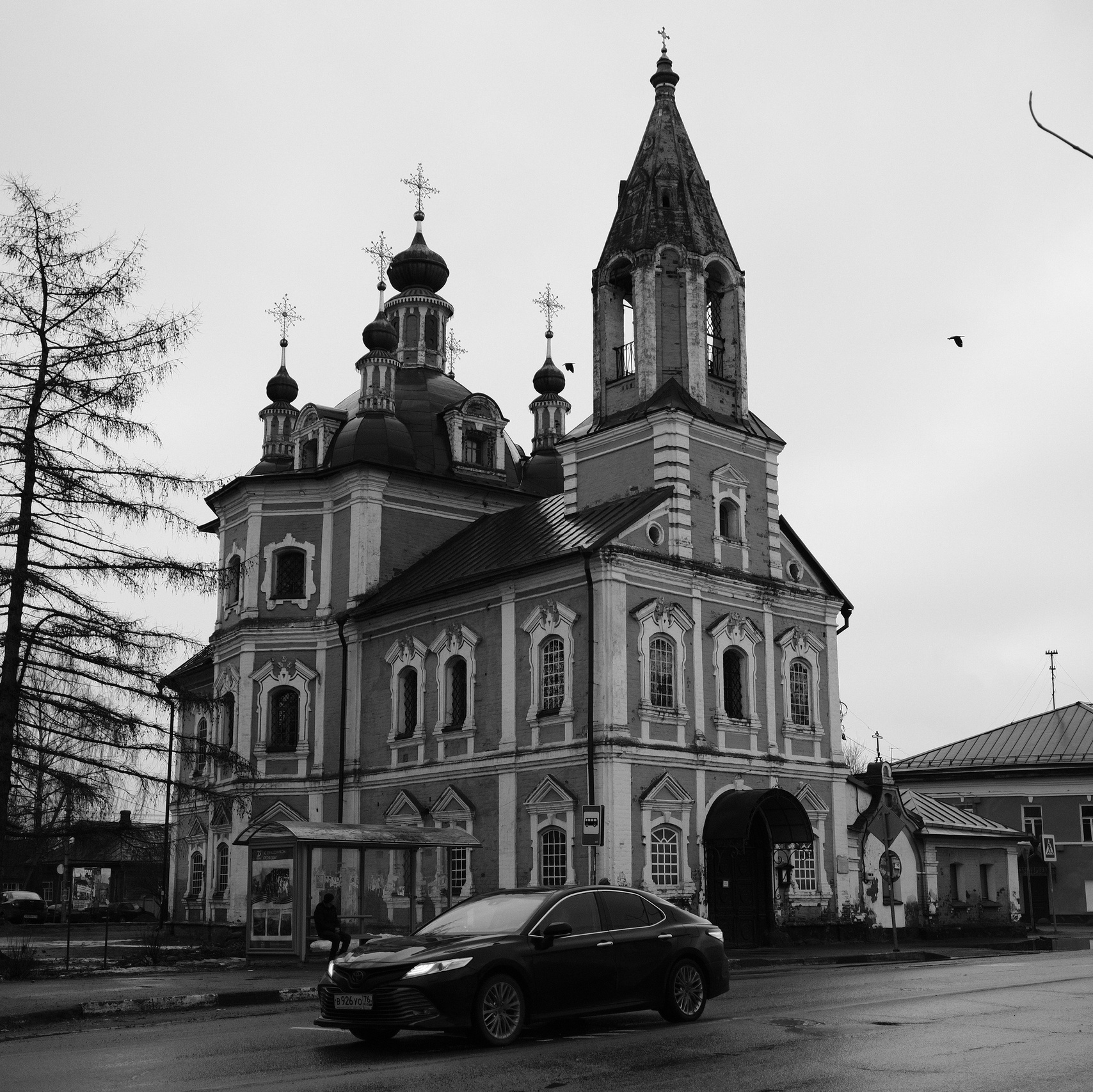 Старинная православная церковь с куполами и колокольней на улице города, машины на переднем плане, черно-белое фото Переславля