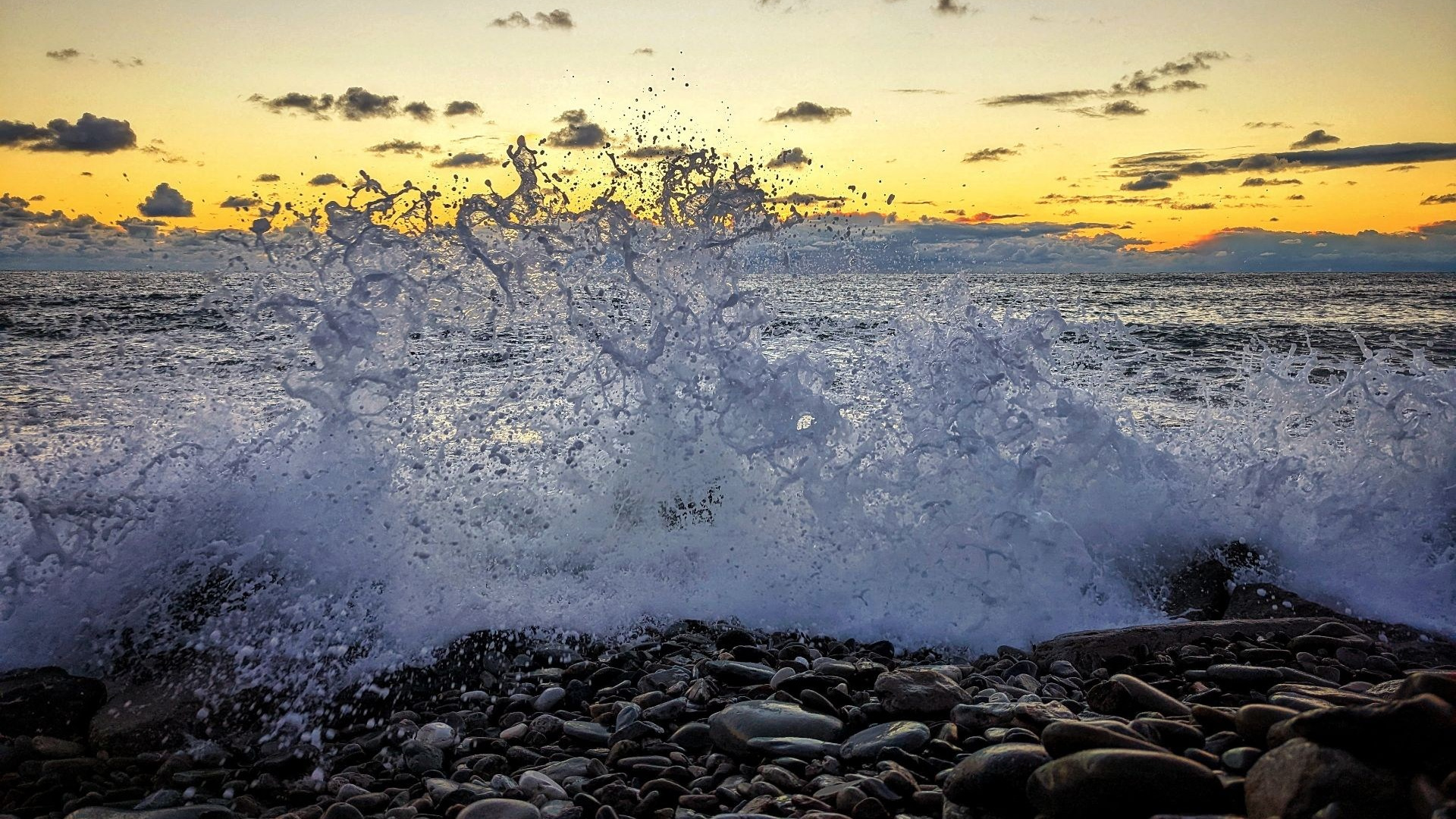 Закат на галечном пляже Черного моря: волны разбиваются о берег, создавая живописный вид