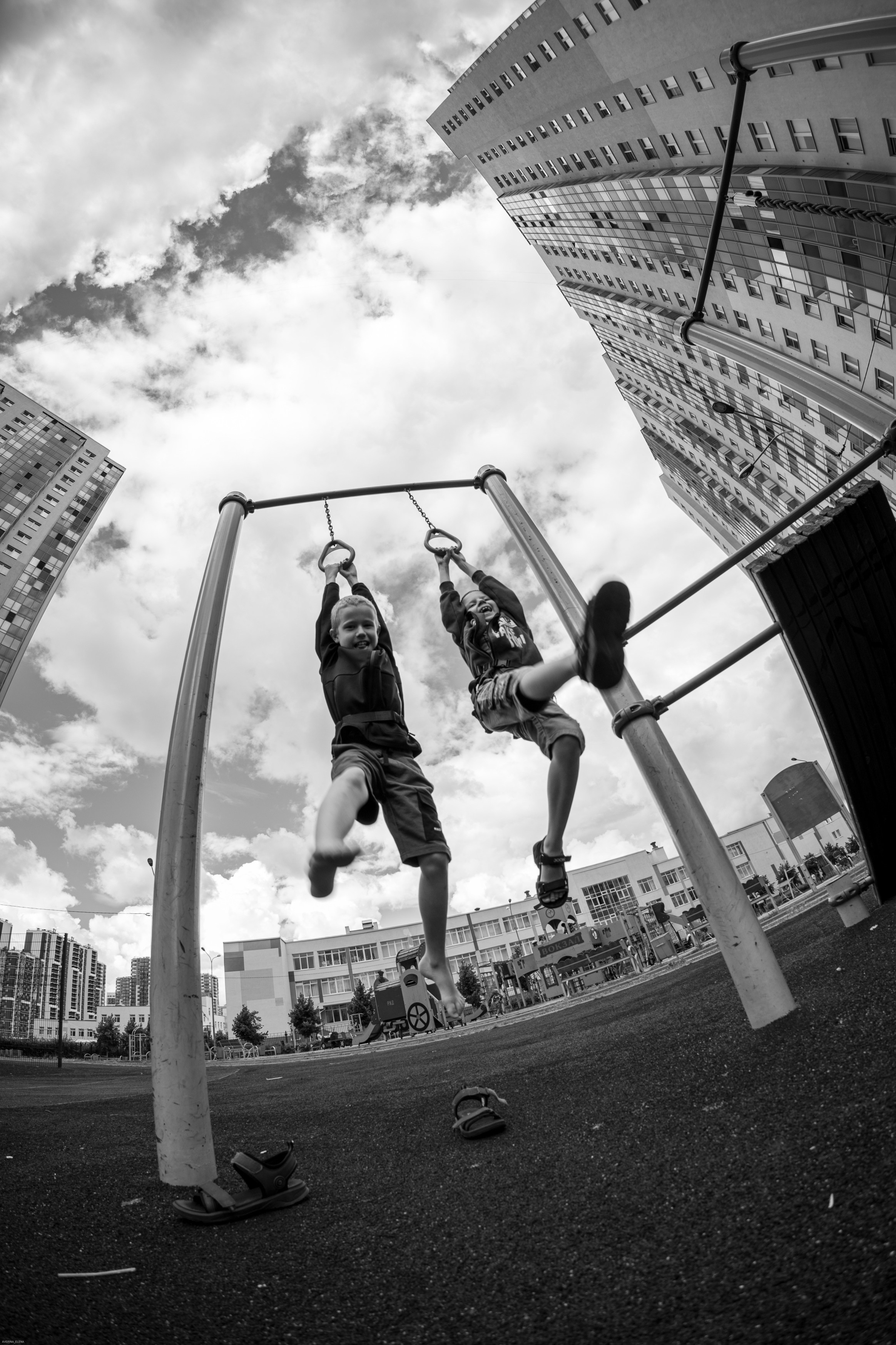 черно-белая фотография во дворе двух мальчиков на детской площадке, которые висят на турнике, съемка на широкоугольный объектив