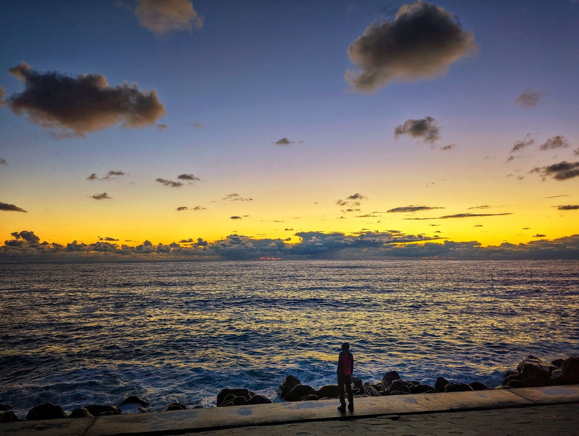 Закат на море с облаками и человеком на набережной