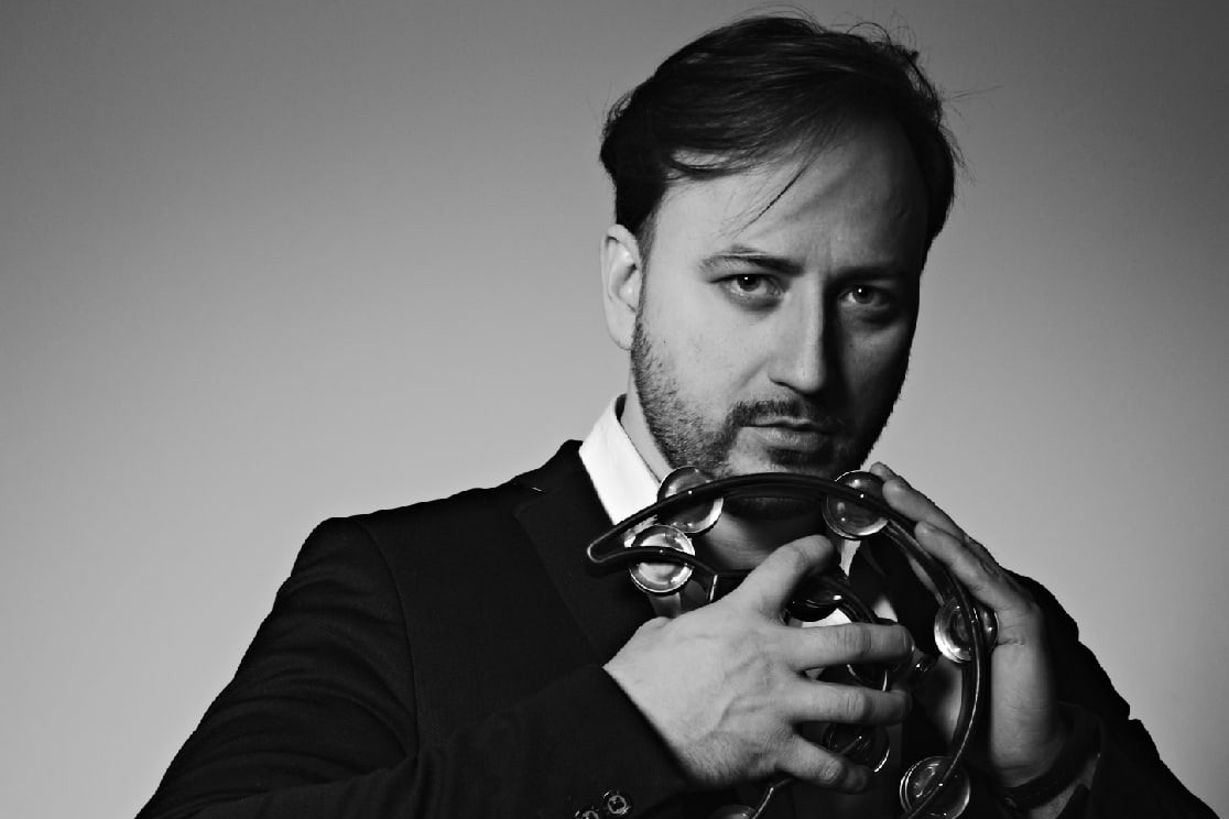 Мужчина в черном пиджаке держит бубен