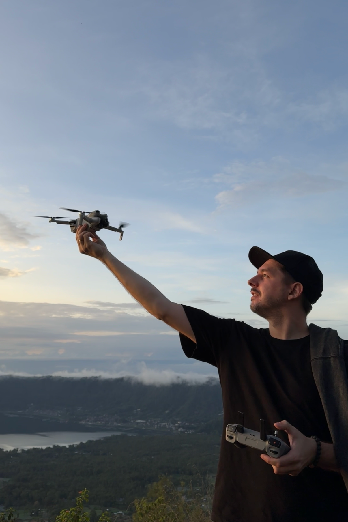 Фотограф Виталий Квант в горах на вулкане на рассвете, силуэт на фоне неба. В руках держит квадрокоптер DJI 