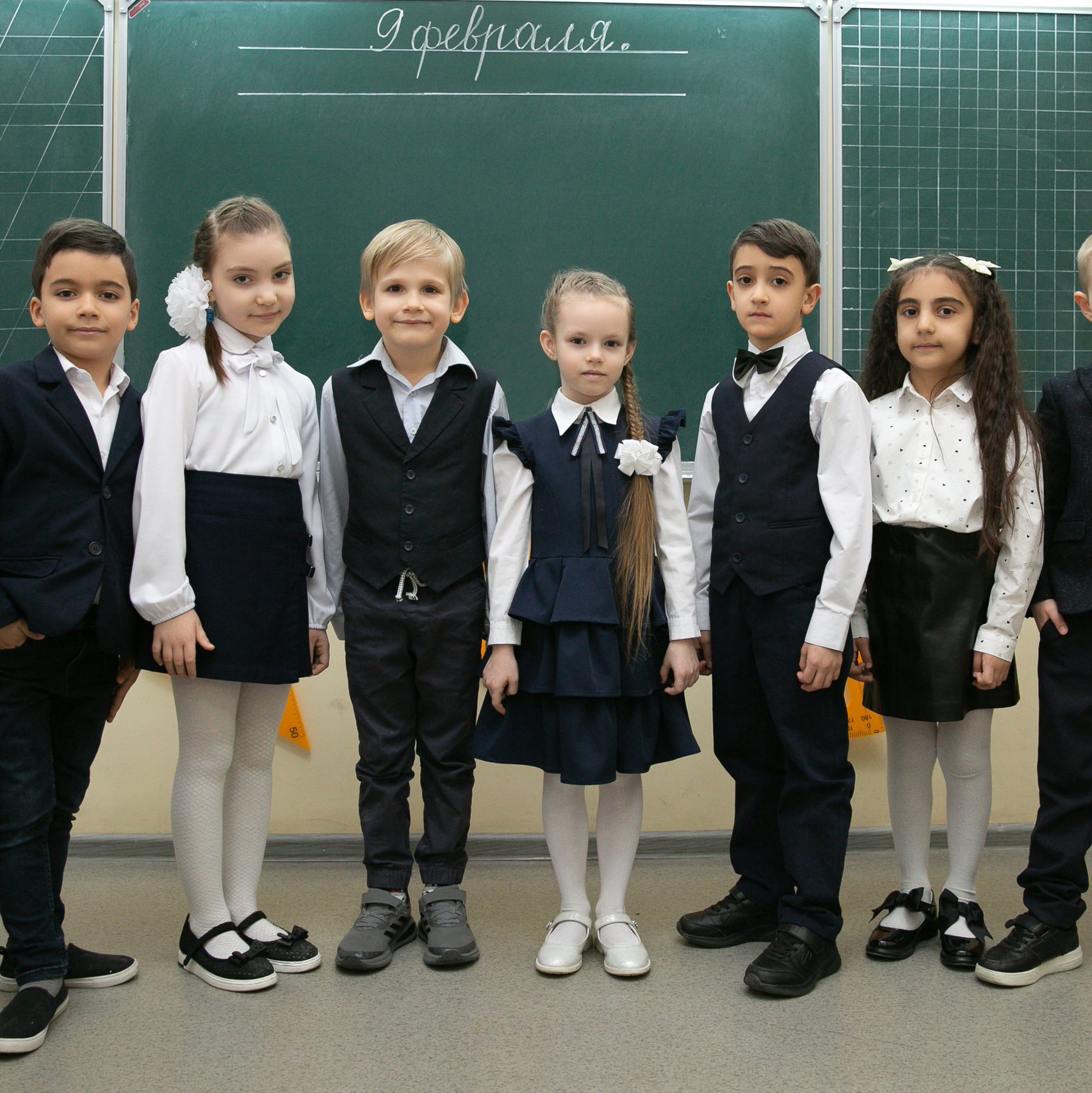 Школьники в форме "галочки" вместе с учителем вшестером стоят у доски.