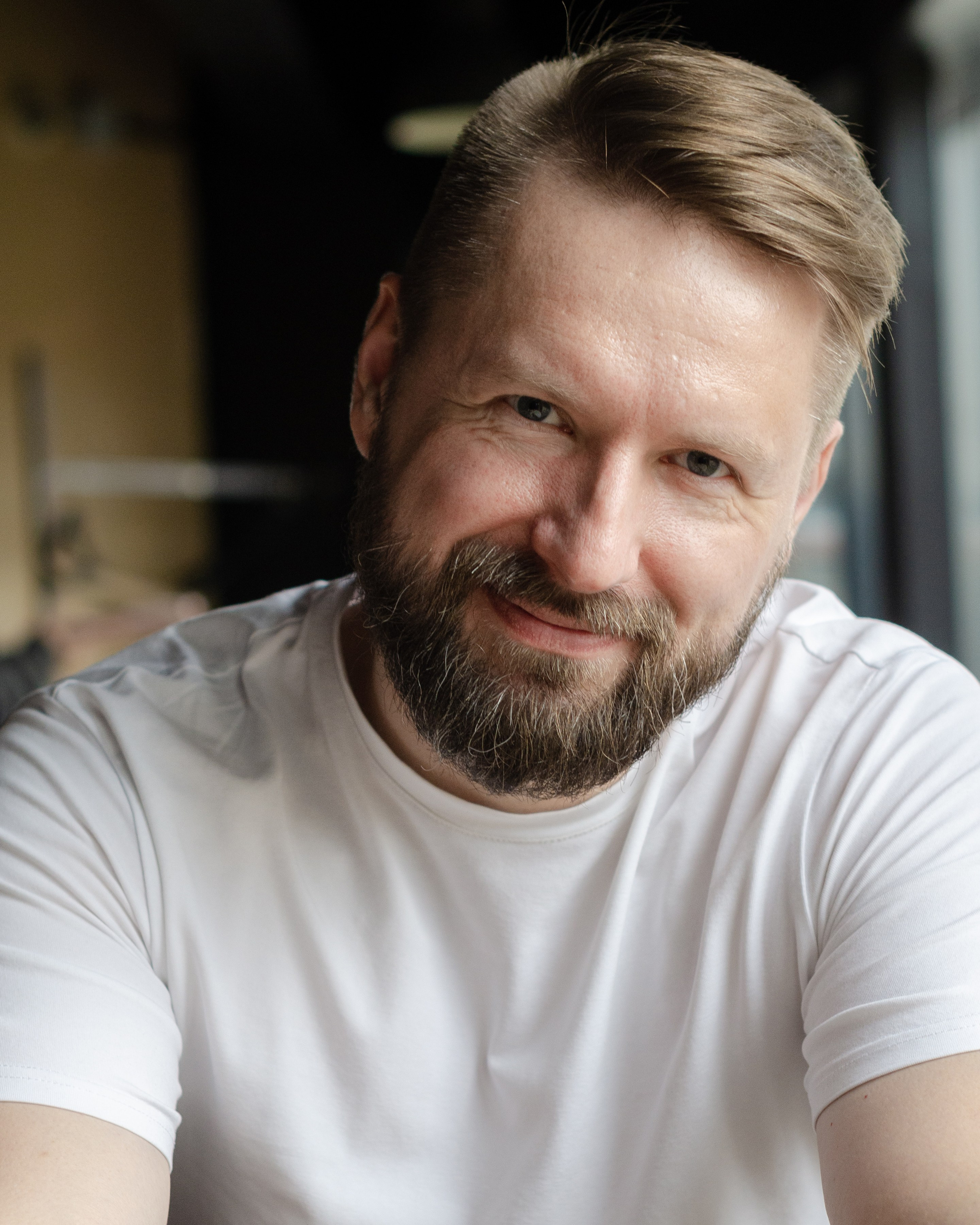 Виктор Кудряшов, фотограф держит в одной руке фотоаппарат, улыбается.