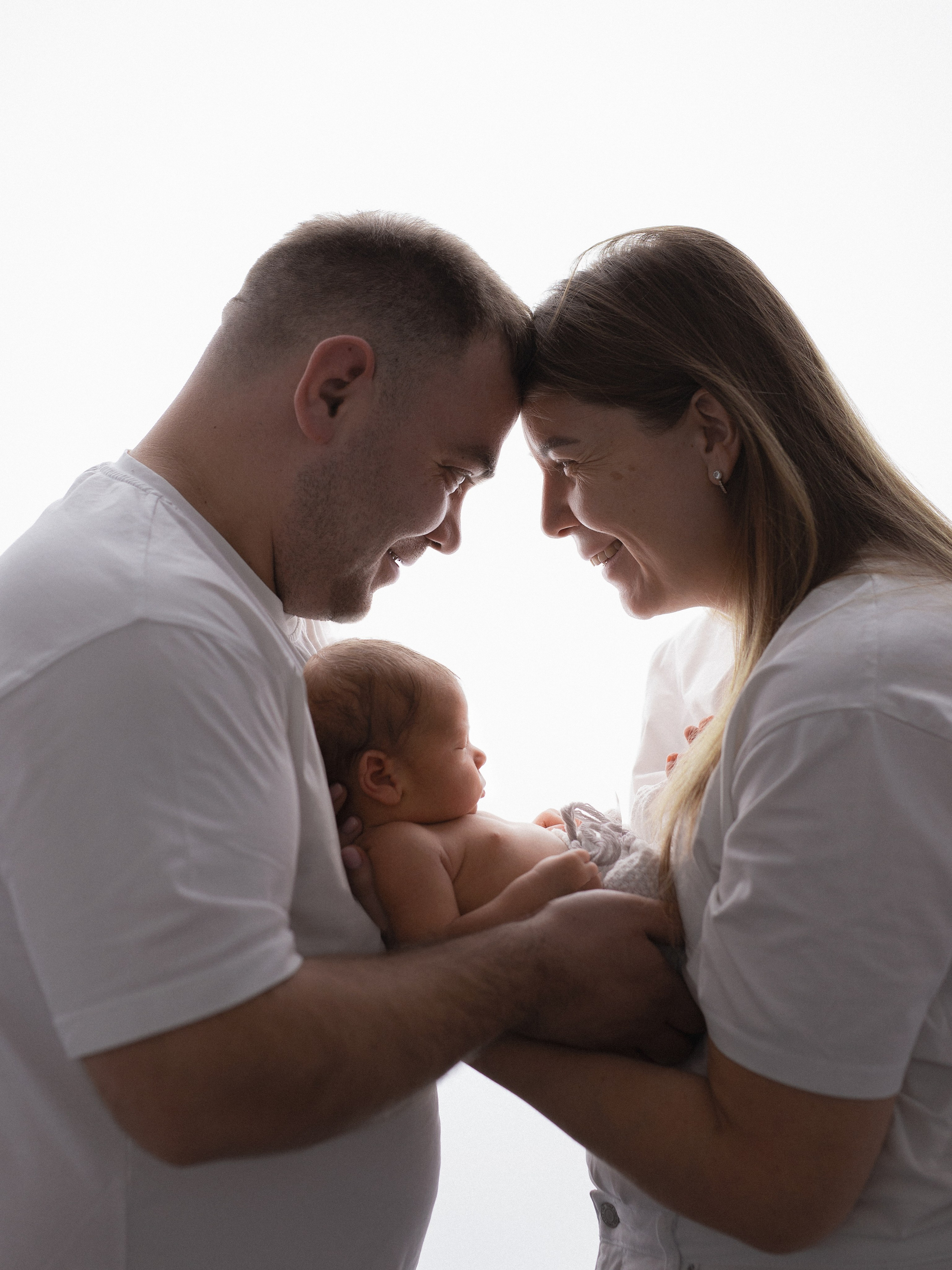 Счастливые родители смотрят на своего малыша в одинаковых белых футболках