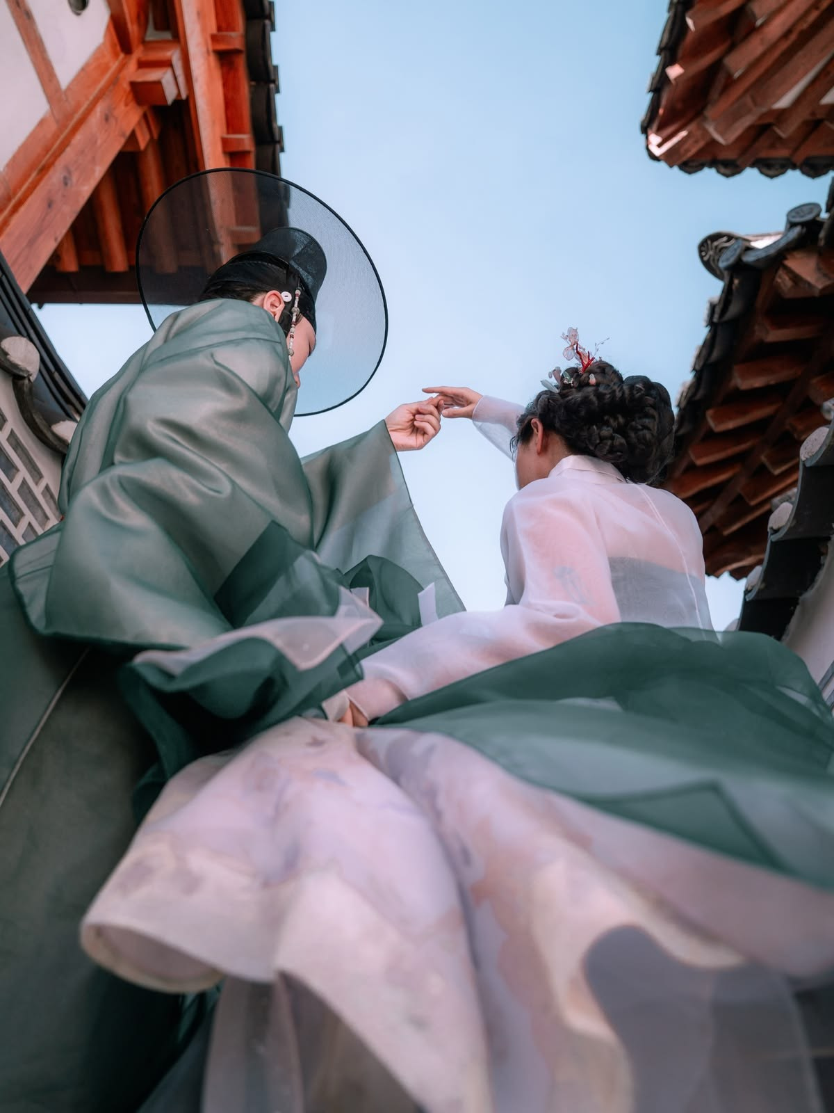 Couple in hanbok twirling under traditional roofs — family hanbok photoshoot in Busan · 감천문화마을