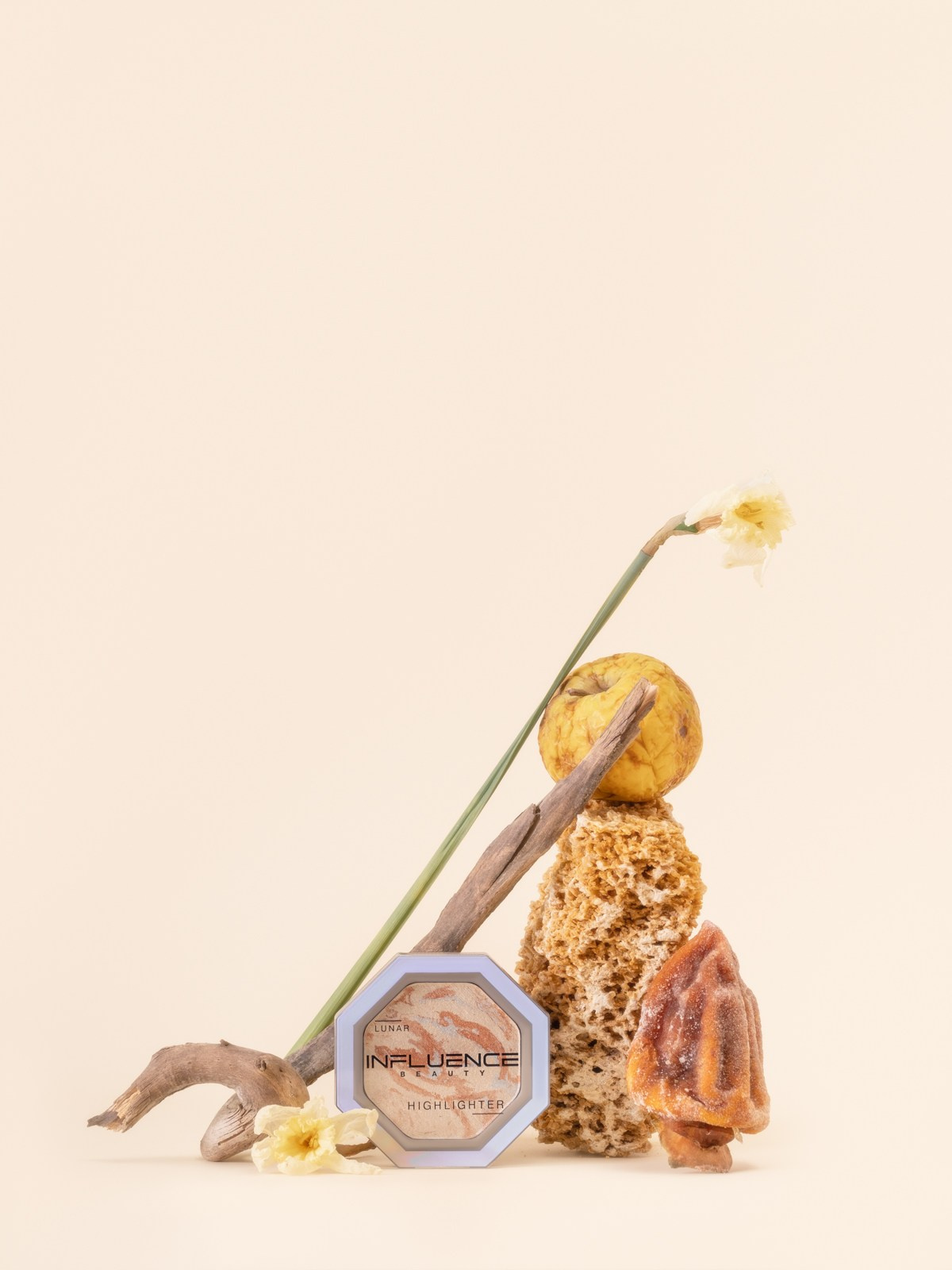 Предметная съёмка хайлайтера Influence Beauty с сухой веткой, губкой, увядшим цветком и сухофруктом на бежевом фоне