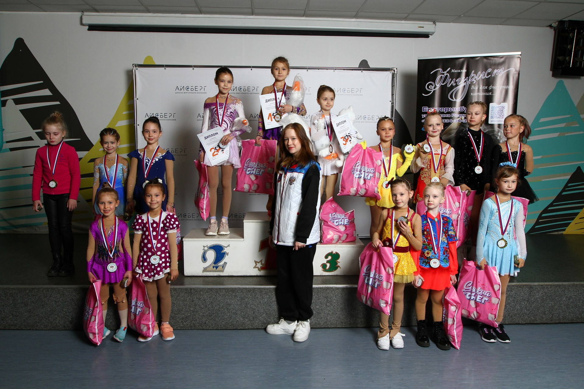 Участники IX Традиционных соревнований по фигурному катанию на коньках «Лунный конек» на церемонии награждения. В руках у спортсменов красочные пакеты "Сладкий снег" от спонсора.  