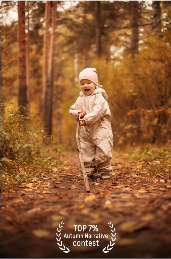 Девочка бежит с палкой в осенних желтых листьях в лесу.