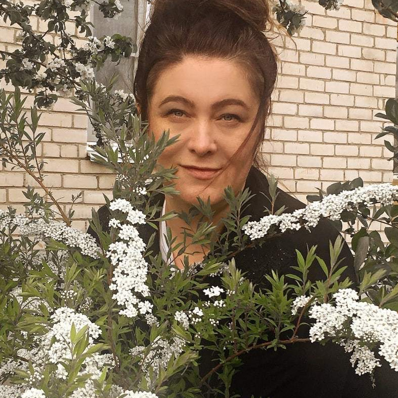 Женщина с рыжими волосами в белой футболке сидит на скамейке