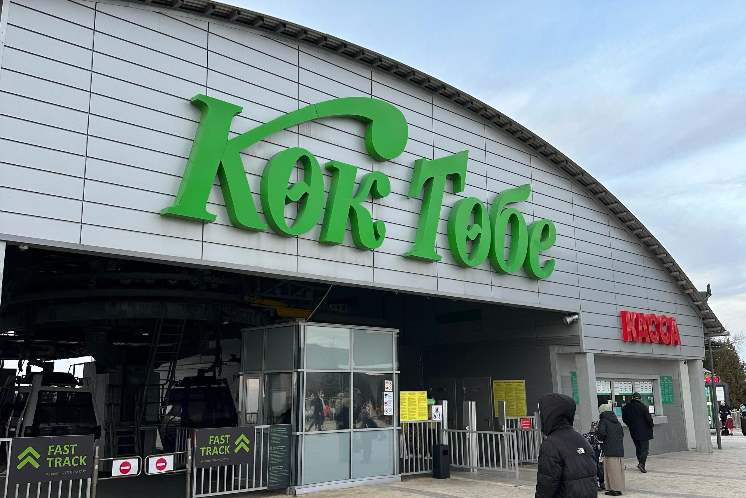 Величественный Чарынский каньон в районе Алматы с ярко-красными скалами, пересечённый извилистой дорогой, на которую падают длинные вечерние тени. Захватывающее сочетание красочных утёсов, зелёных склонов и драматичного неба создаёт эффектный пейзаж