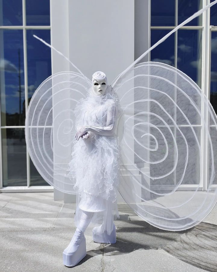 Мим в образе белой бабочки на встрече гостей у ресторана.