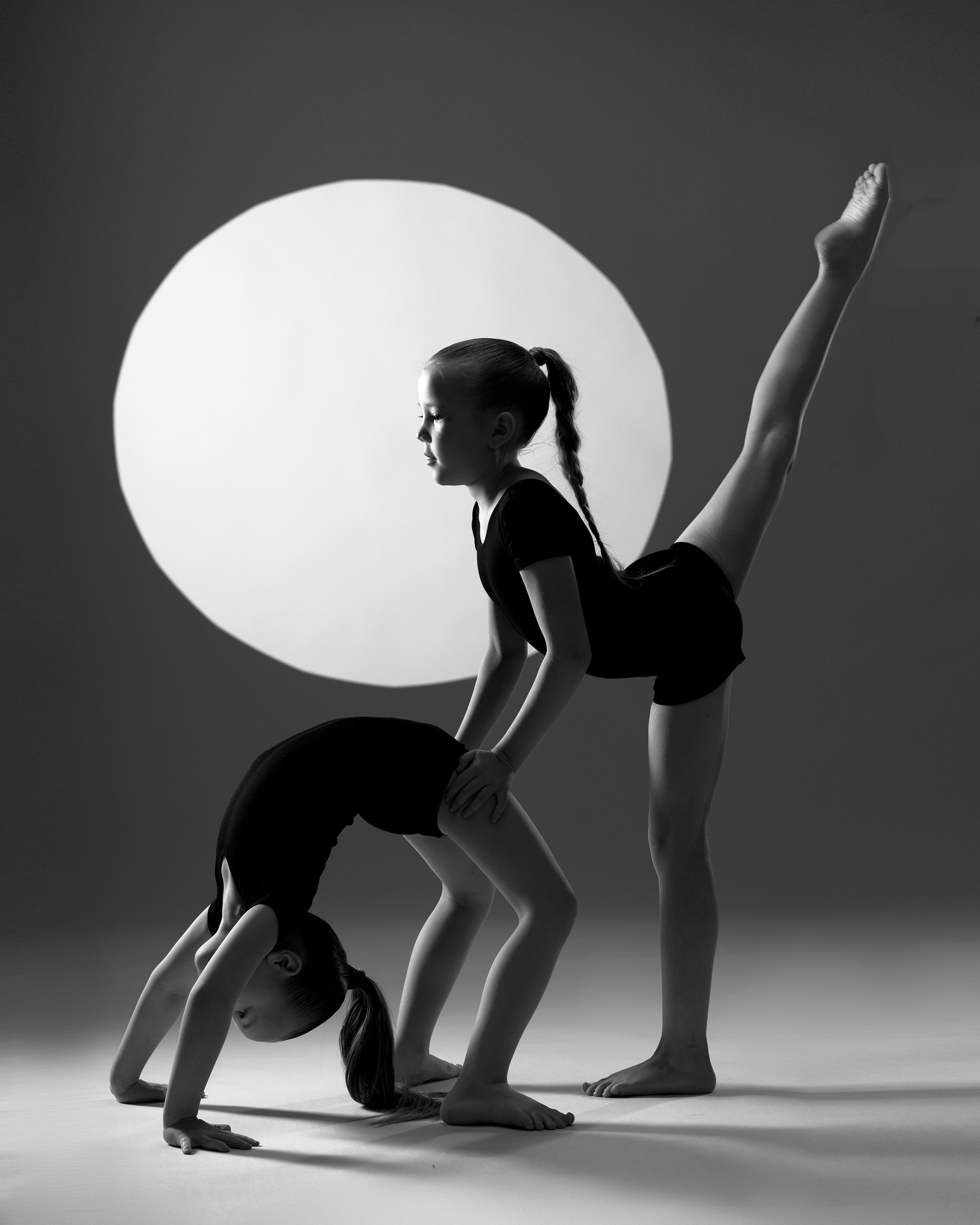 Художественное черно-белое фото юных гимнасток в акробатических позах, студийная съемка в жанре спортарт с графичным светом.