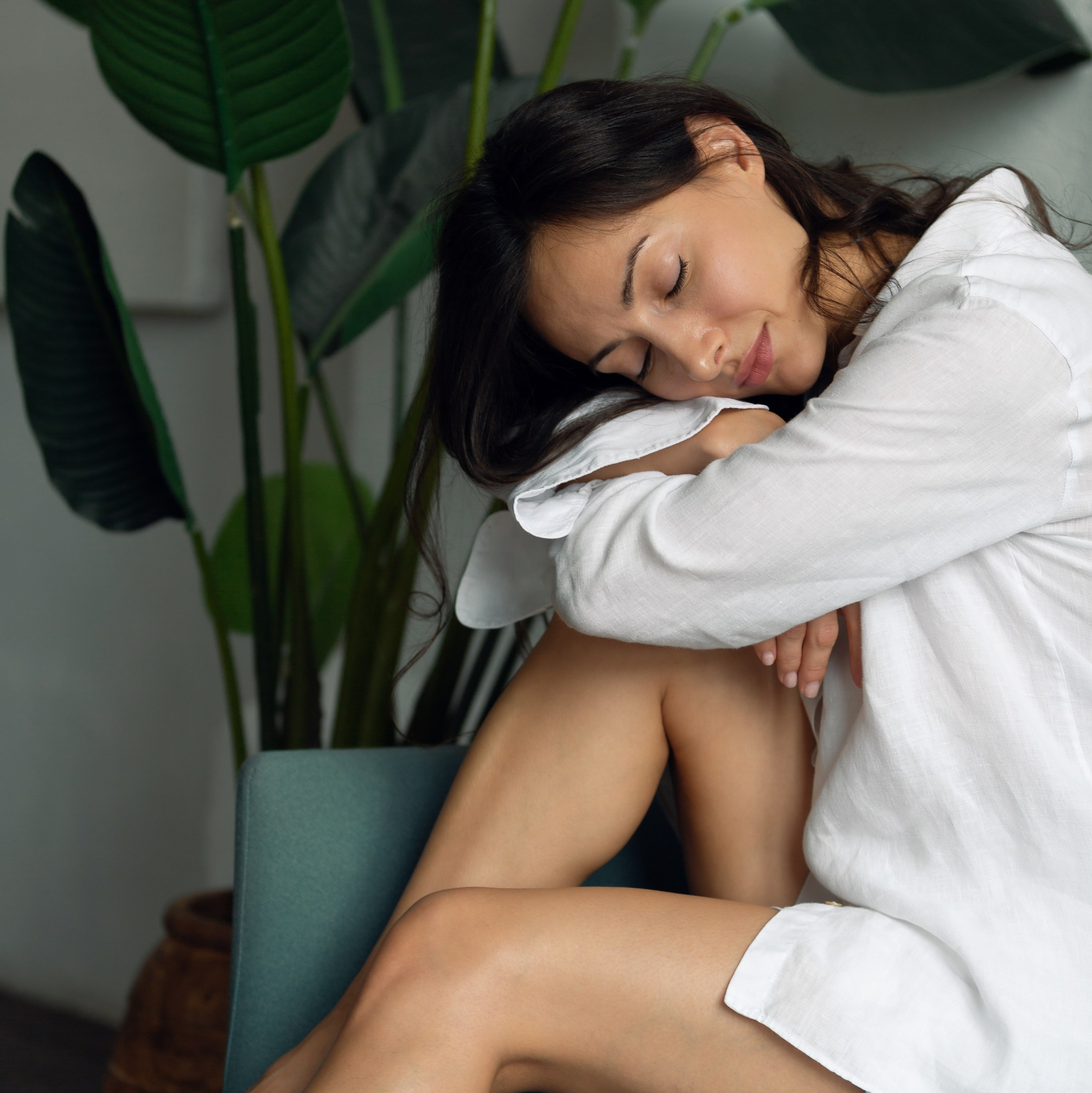 Девушка в белой рубашке улыбается, сидя на стуле возле растений. Лёгкая фотосессия в подарок.